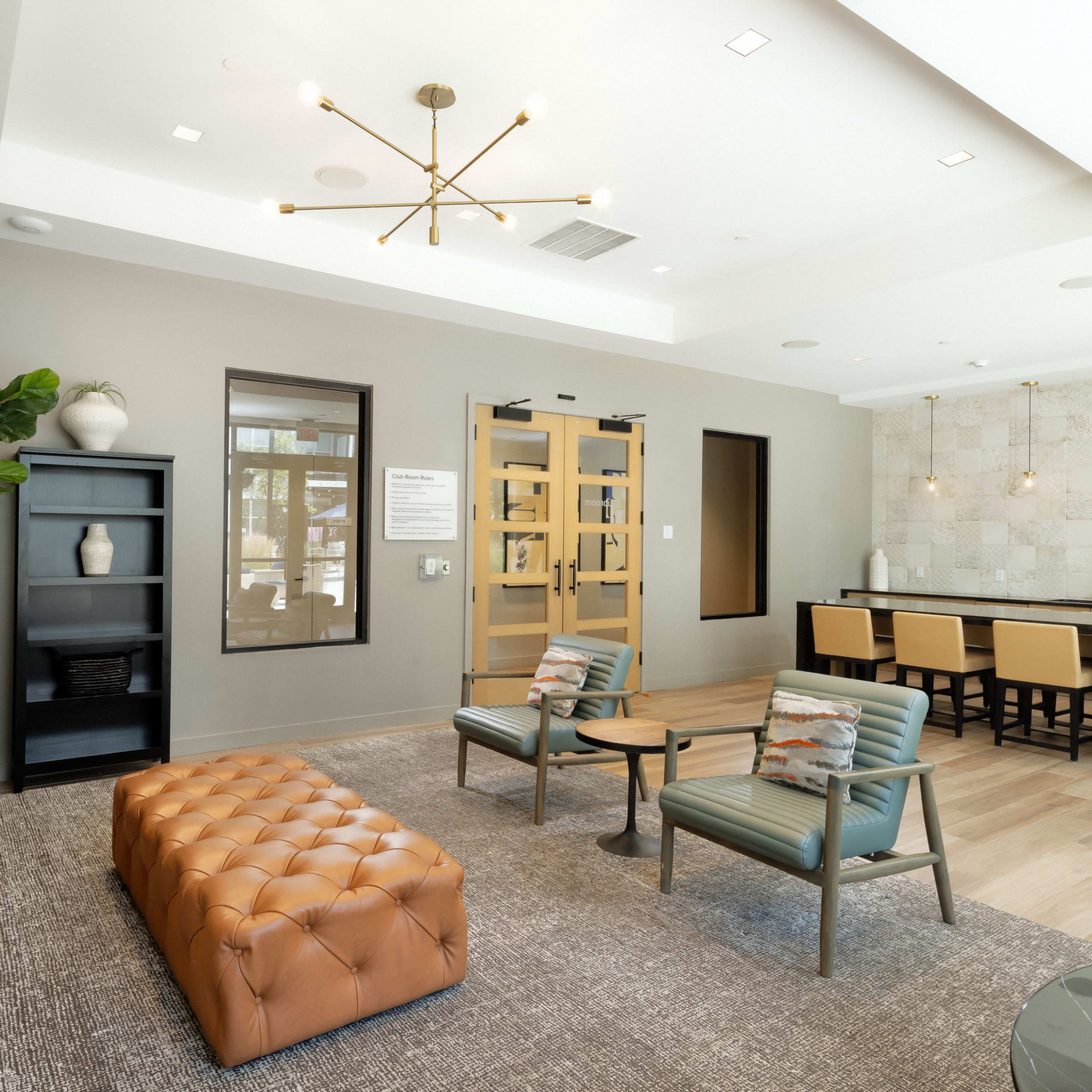 A modern lobby area with a tufted leather ottoman, seating, and a service counter, featuring neutral colors and decorative elements.