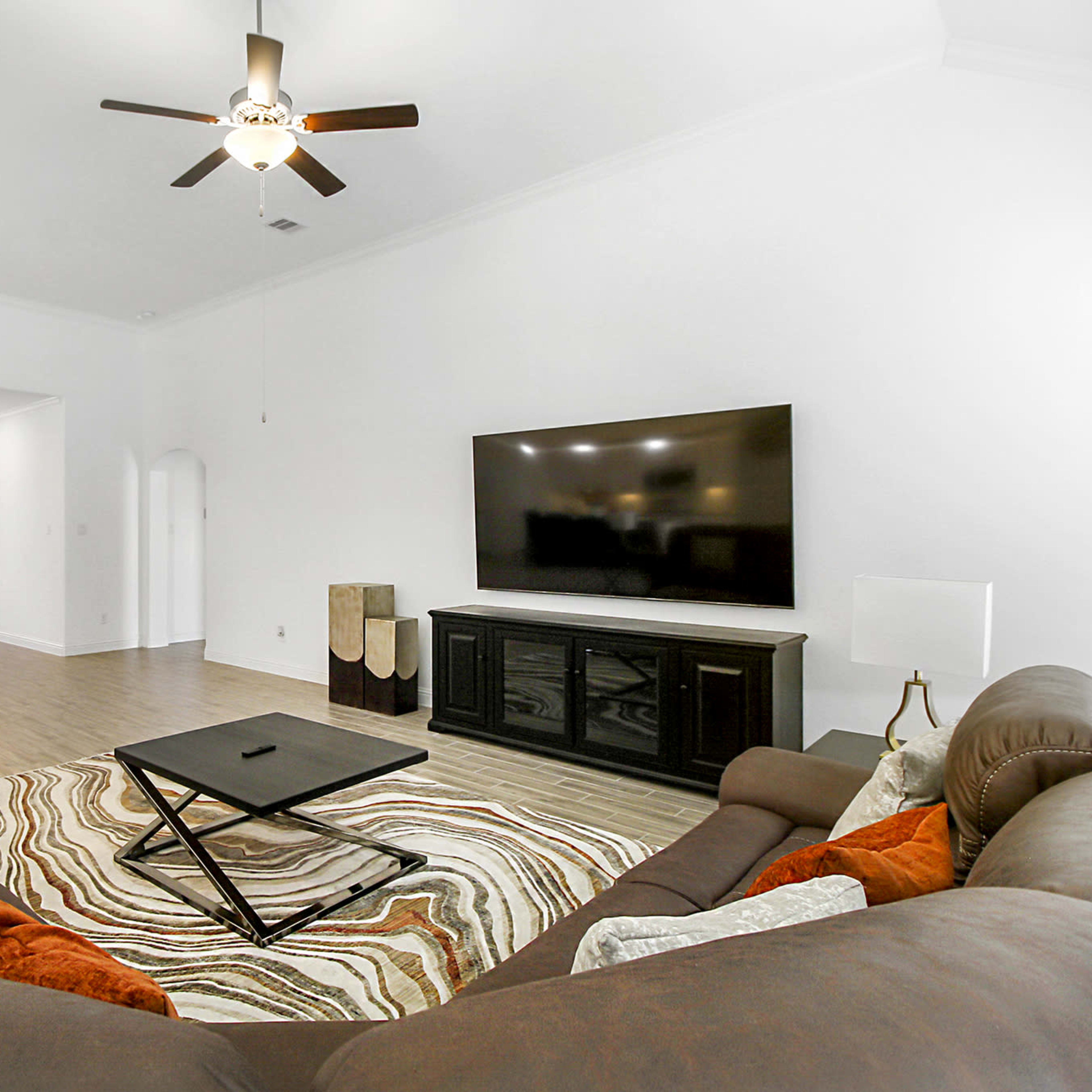 The living room features a large brown sectional sofa, a coffee table, and a wall-mounted television, with a dining area visible in the background.