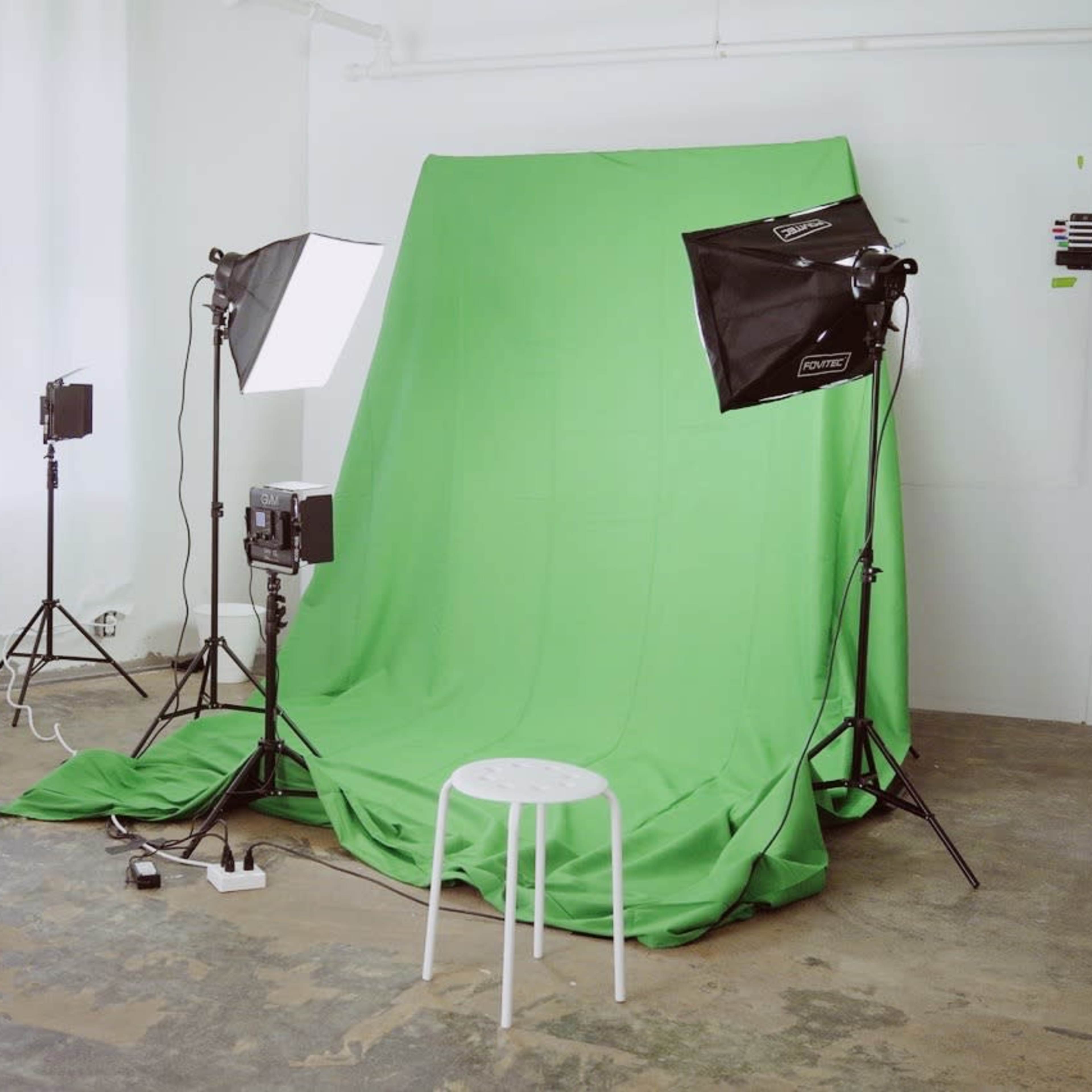 A photography setup featuring a green backdrop, two studio lights, and a small white stool in a well-lit room.