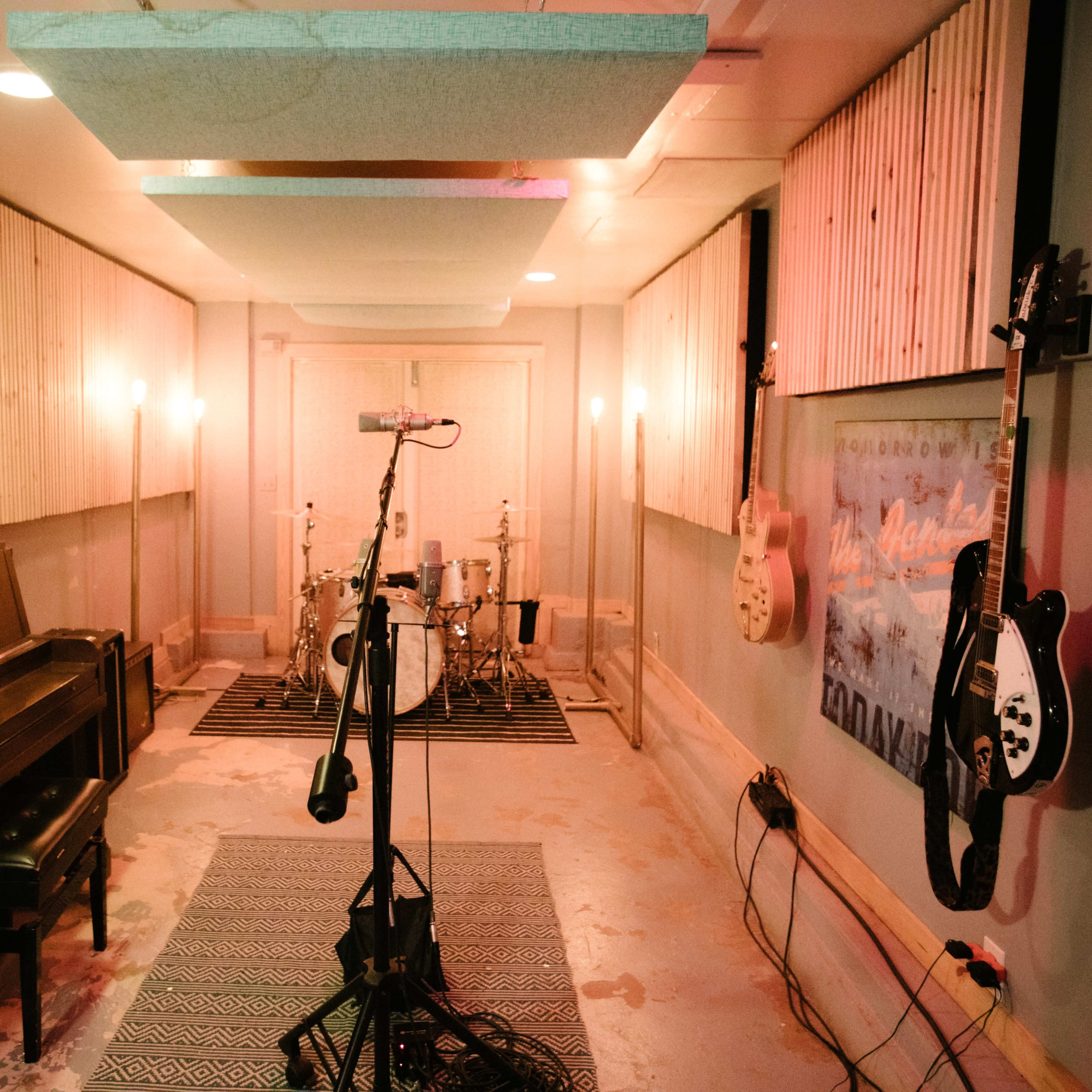 A music recording studio featuring a piano, a drum set, and electric guitars mounted on the wall.