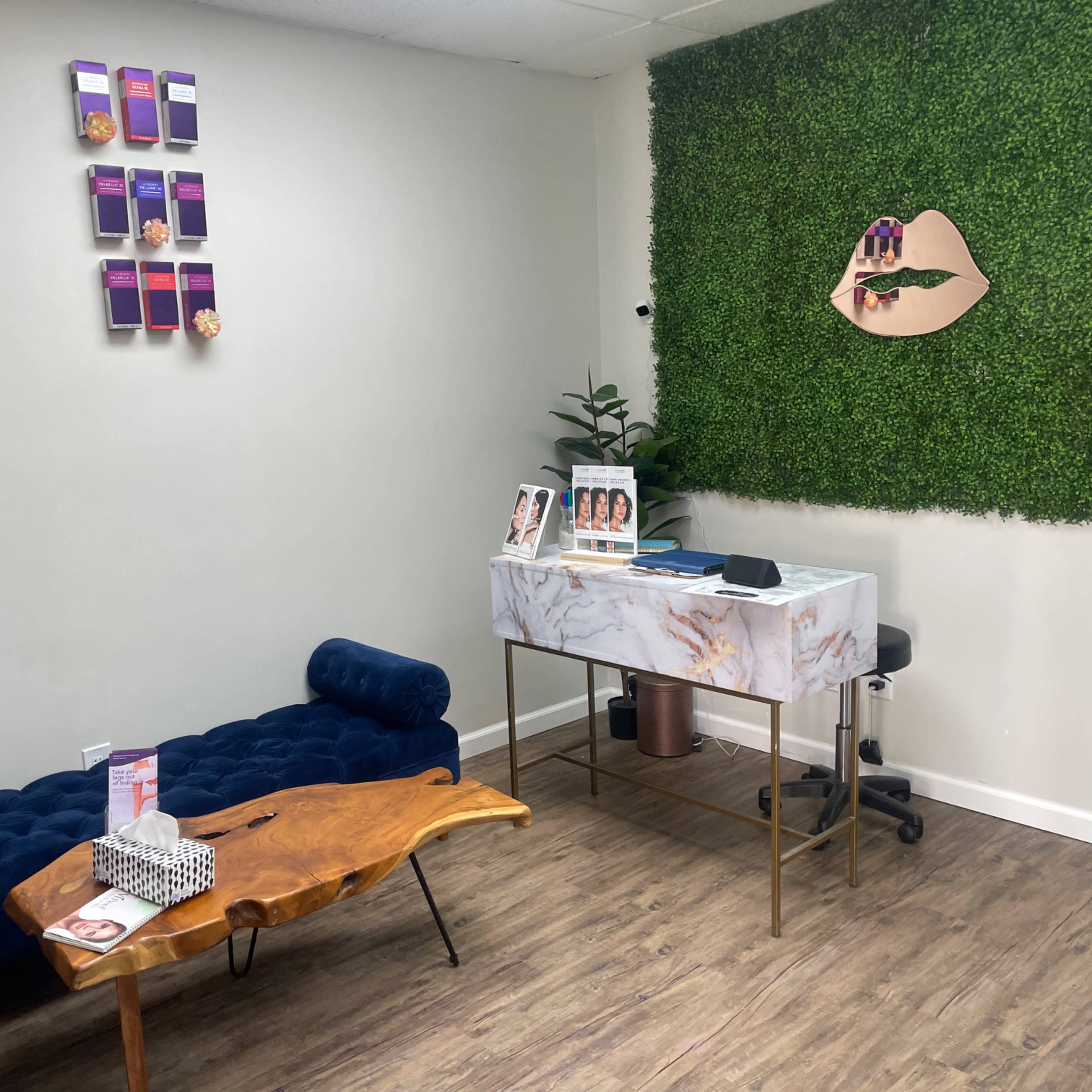 A stylish reception area with a blue velvet couch, a wooden coffee table, and a marble reception desk against a backdrop of green foliage.