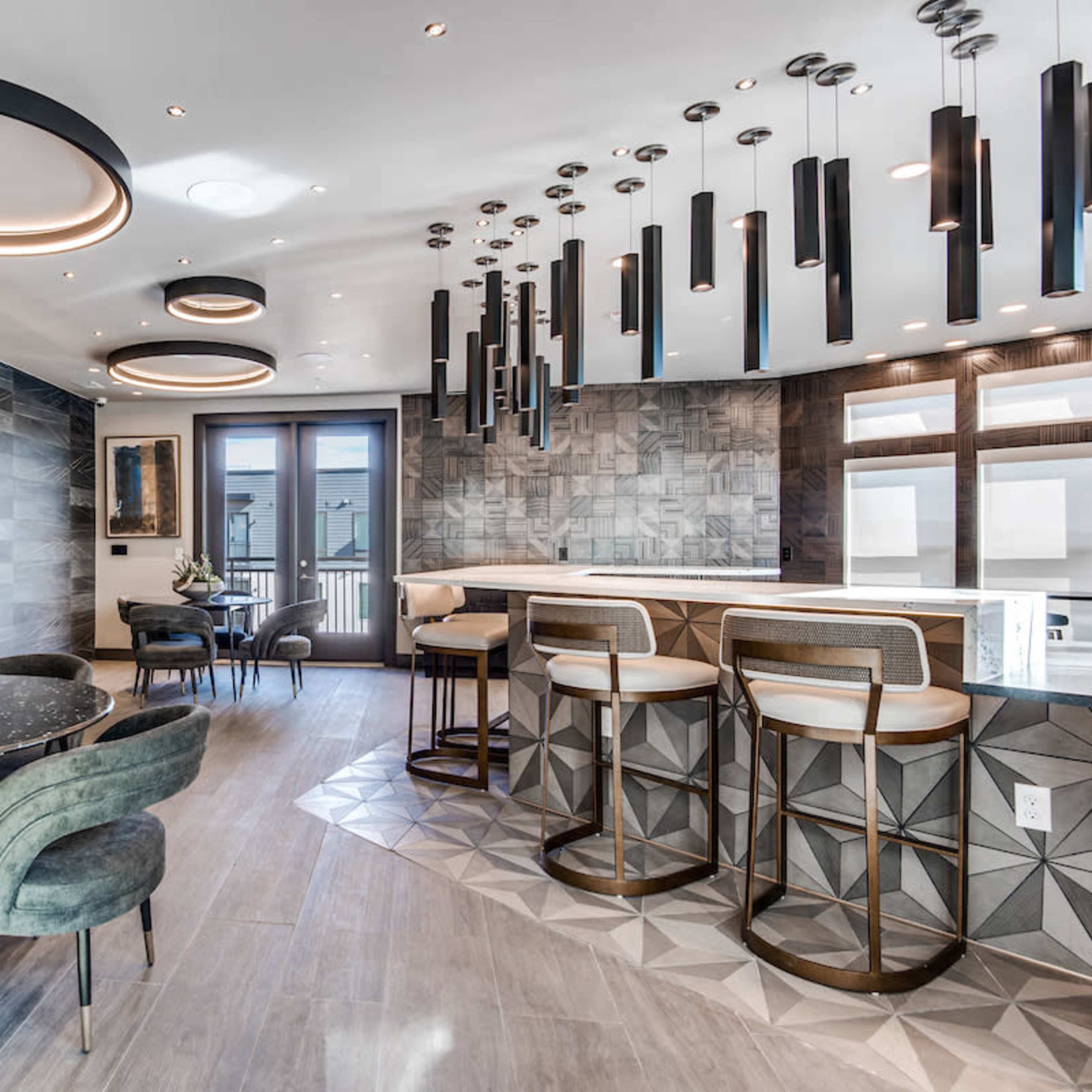 A modern kitchen and dining area featuring a circular table with upholstered chairs, a sleek bar with high stools, and multiple pendant lights hanging from the ceiling.