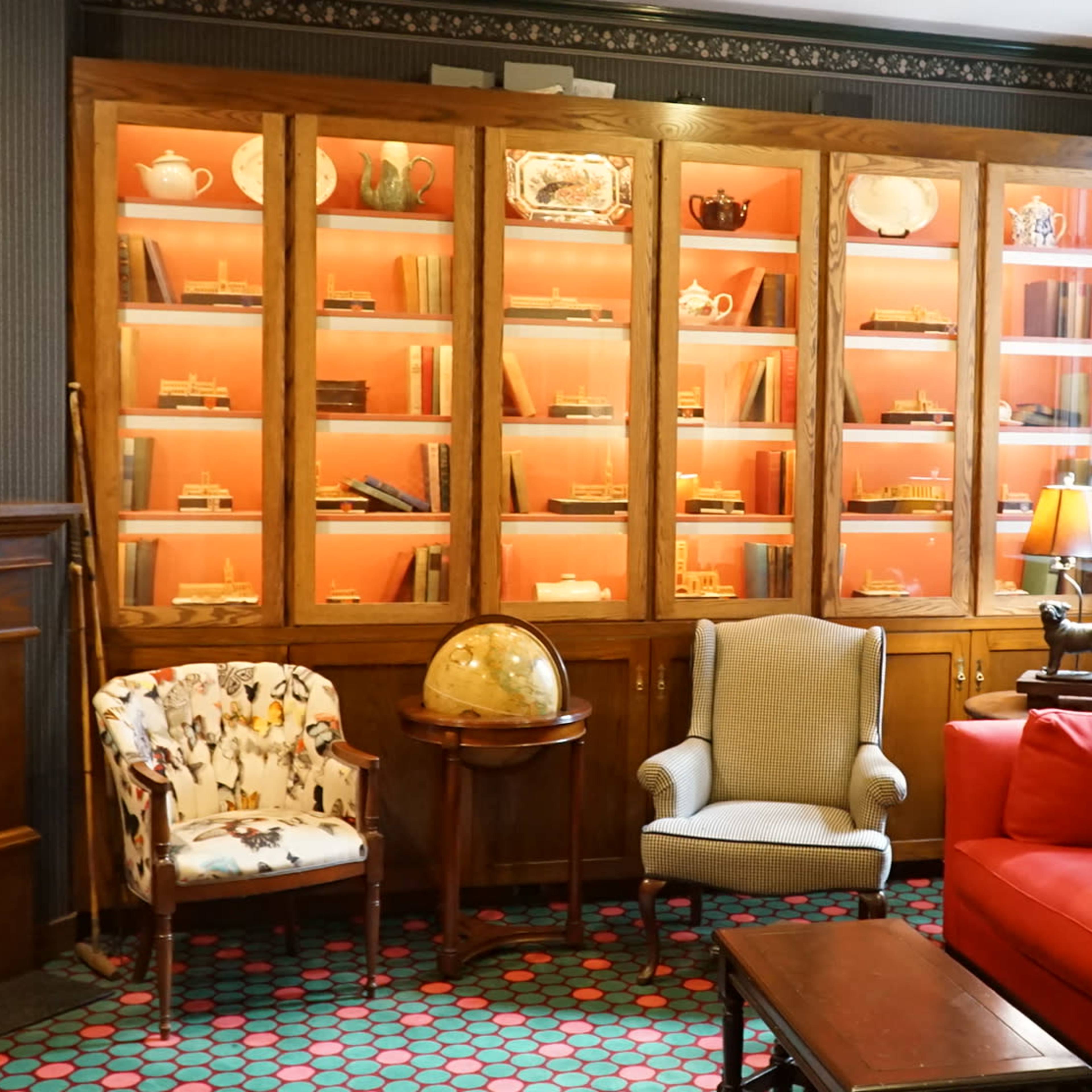 A cozy room with a red couch, two armchairs, and a display cabinet filled with items, illuminated by soft pink lighting.