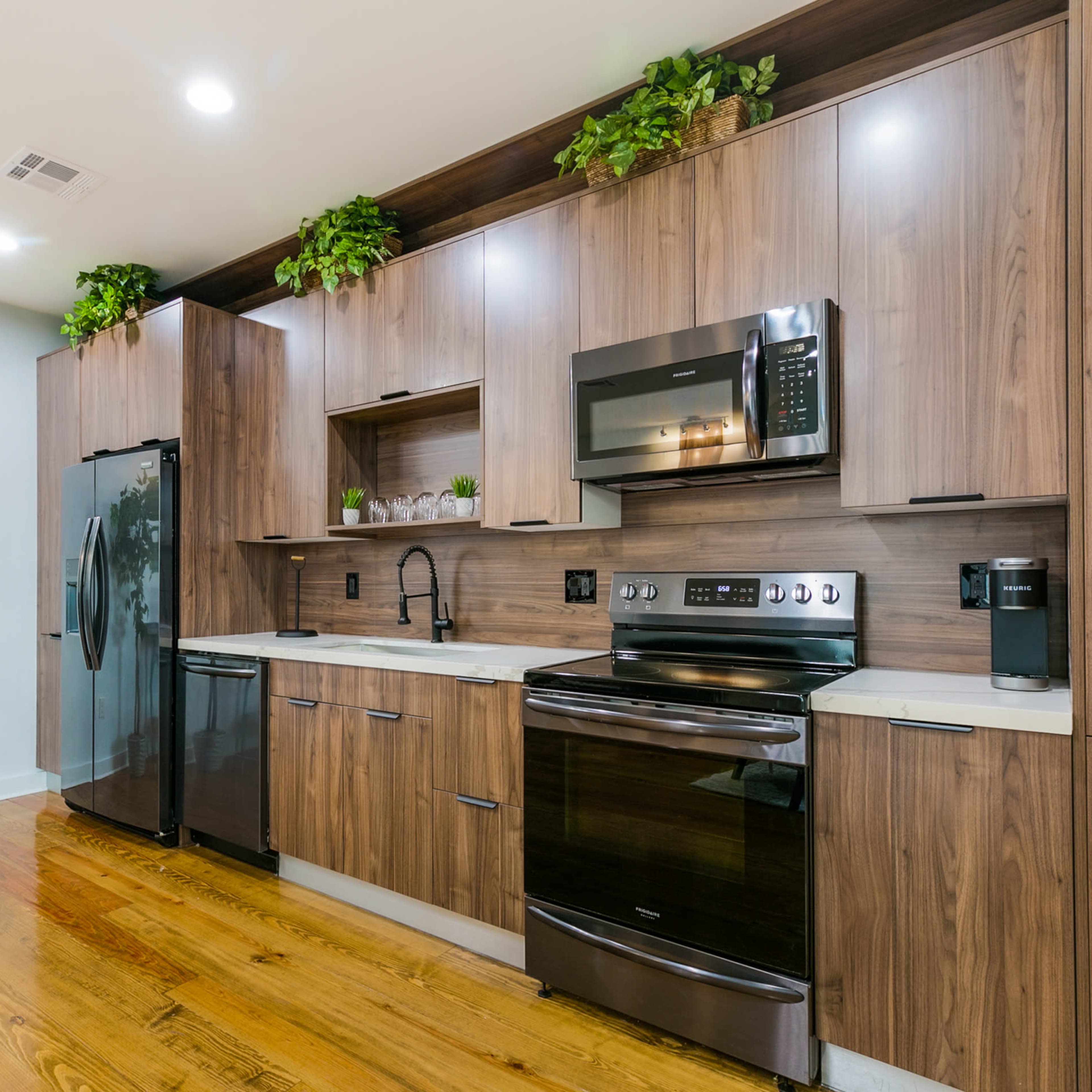 A modern kitchen with wooden cabinetry, a black refrigerator, and stainless steel appliances.