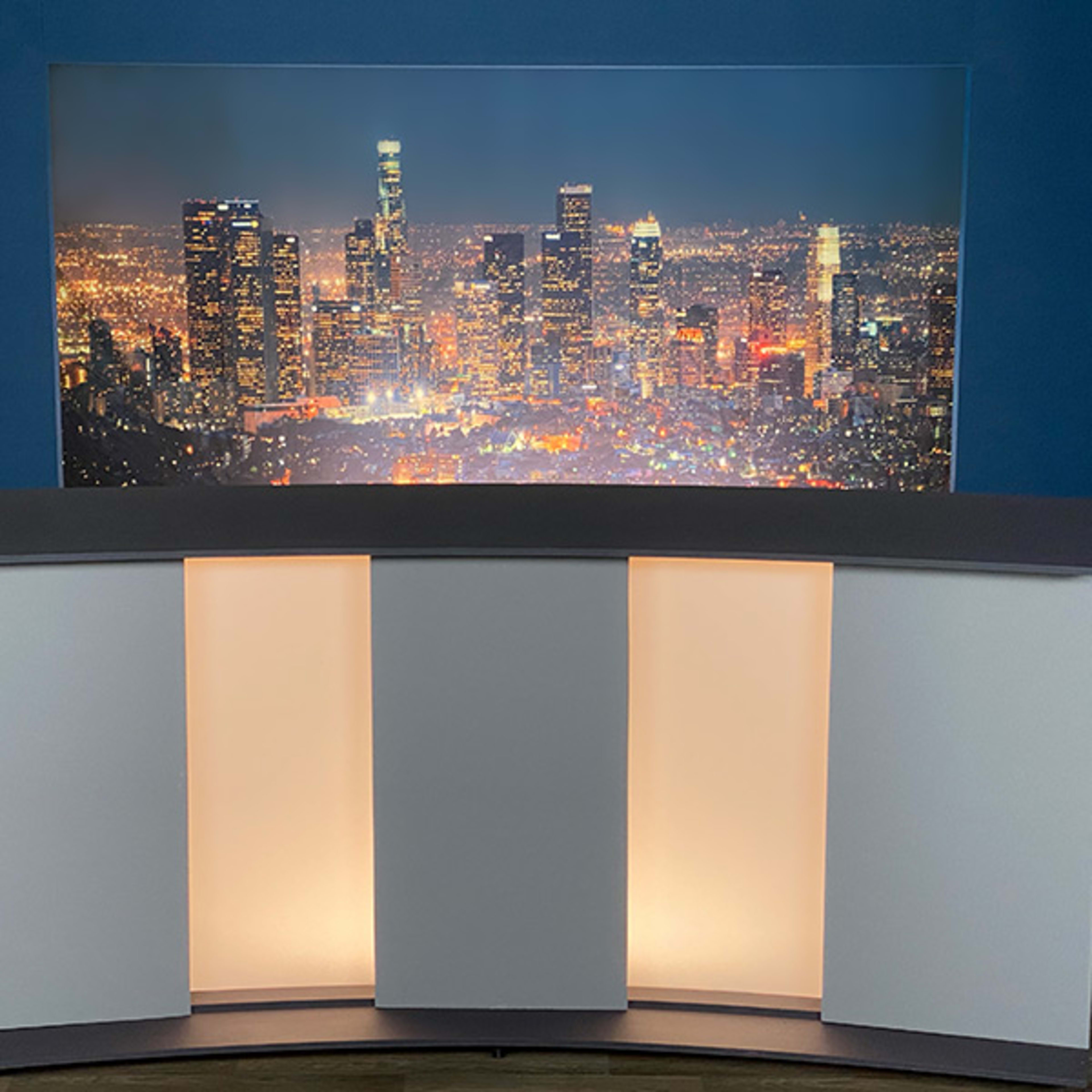 A modern broadcasting studio setup featuring a curved counter in front of a backdrop displaying a nighttime city skyline with bright lights.
