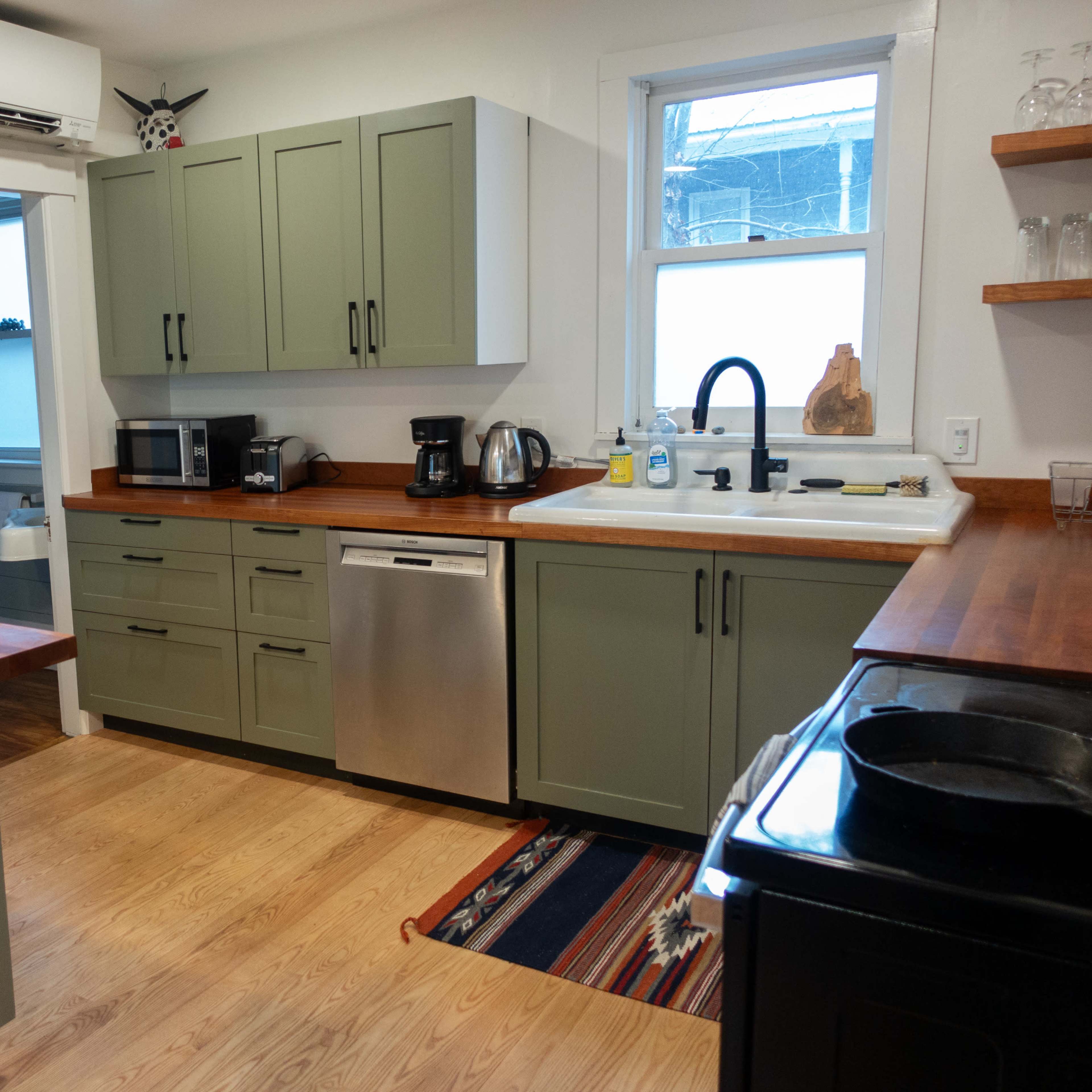 The kitchen features green cabinets, stainless steel appliances, and wood countertops with a rug near the sink.