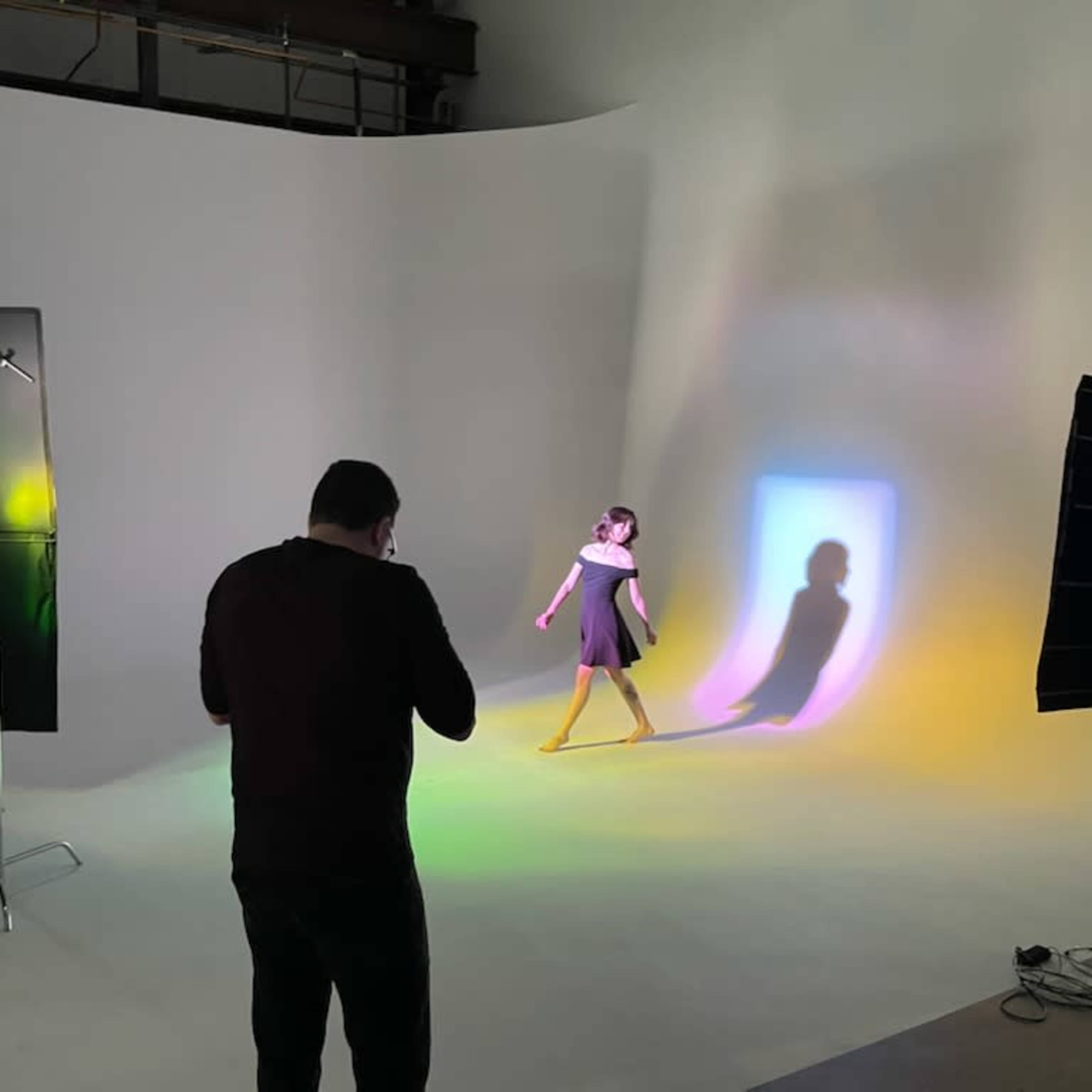 A model poses under colorful lights in a studio while a photographer captures the moment.