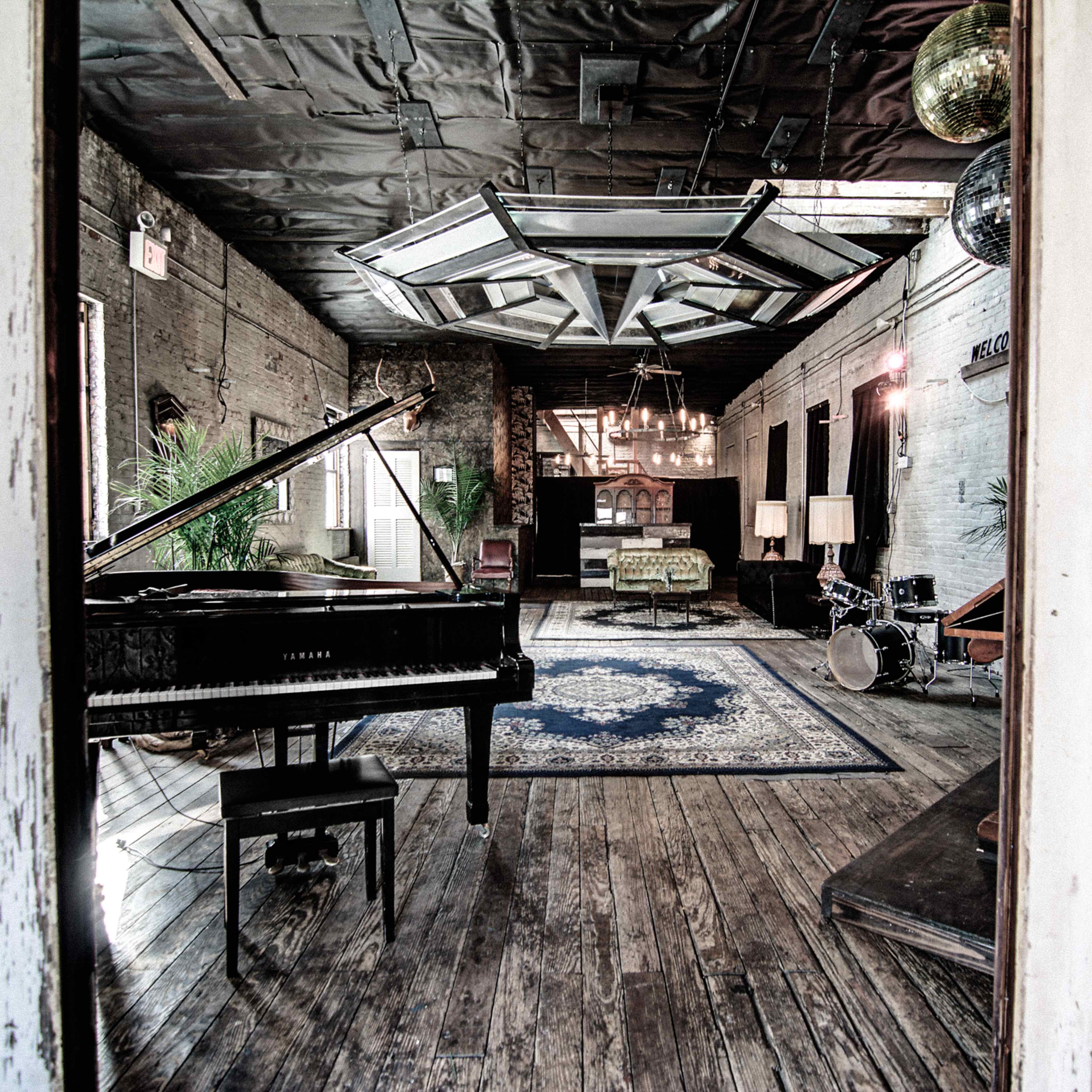 A spacious room featuring a grand piano, a patterned rug, various seating areas, and decorative lighting.