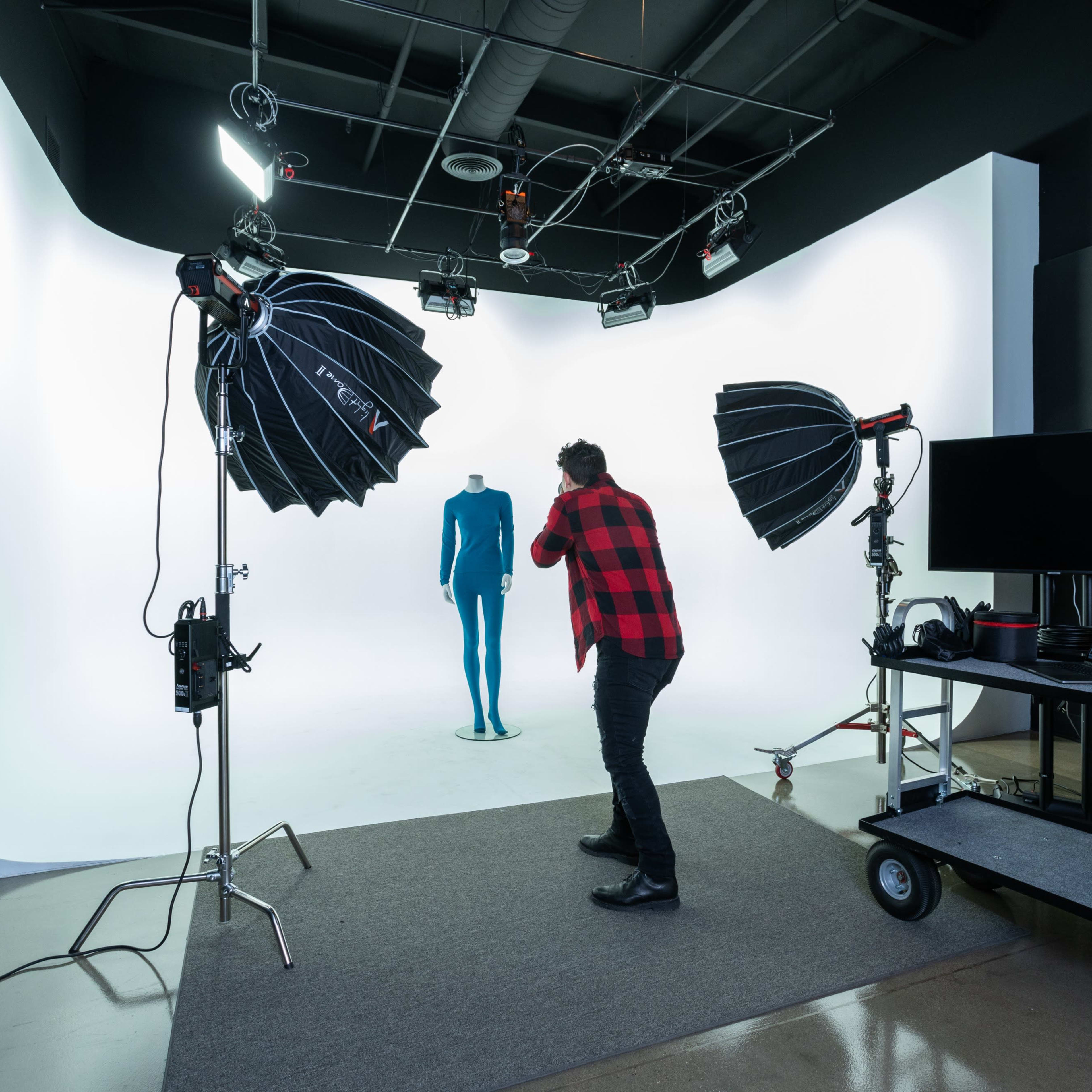 A photographer adjusts lighting equipment in a studio featuring a backdrop and a mannequin.