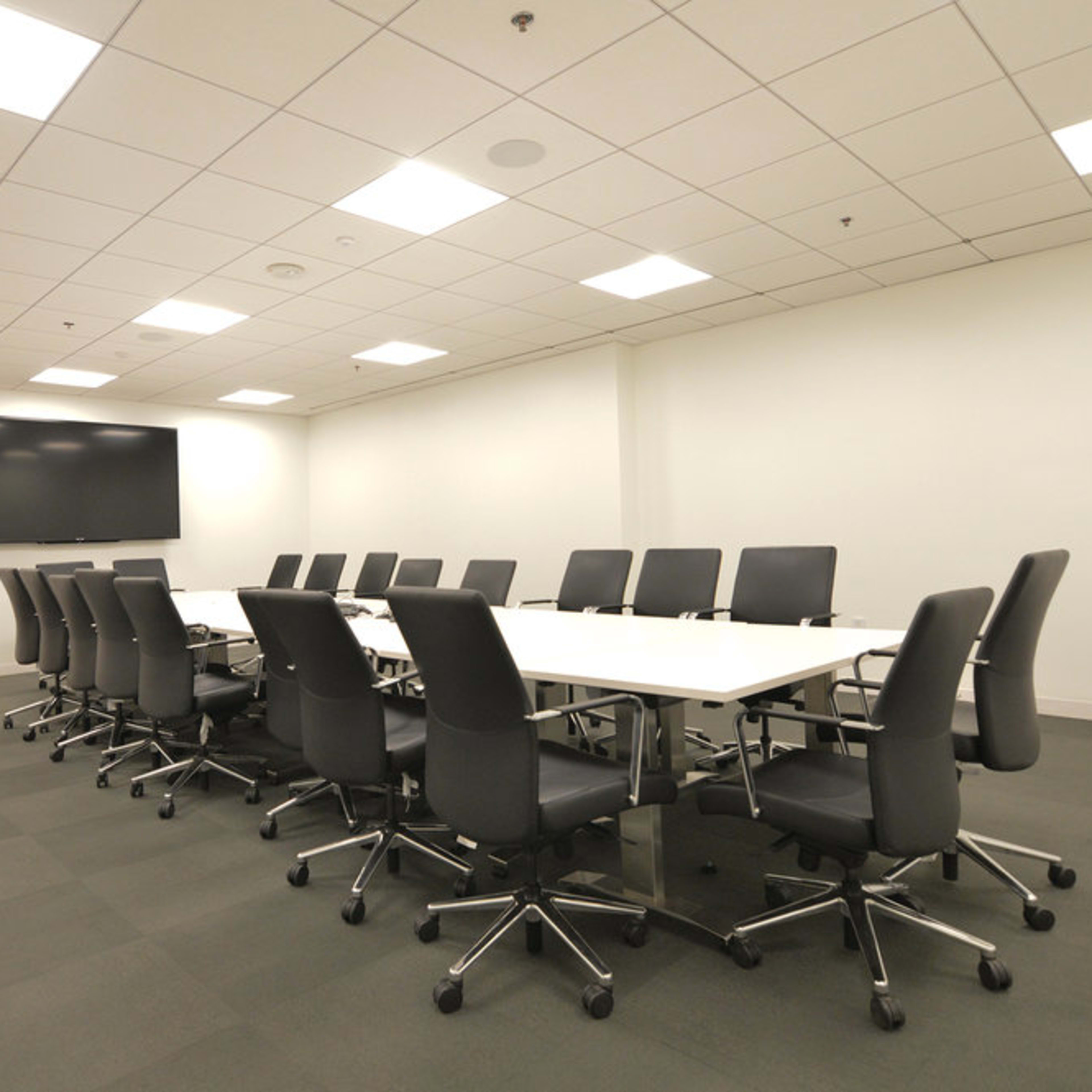 A conference room features a long table surrounded by office chairs and a large television mounted on the wall.