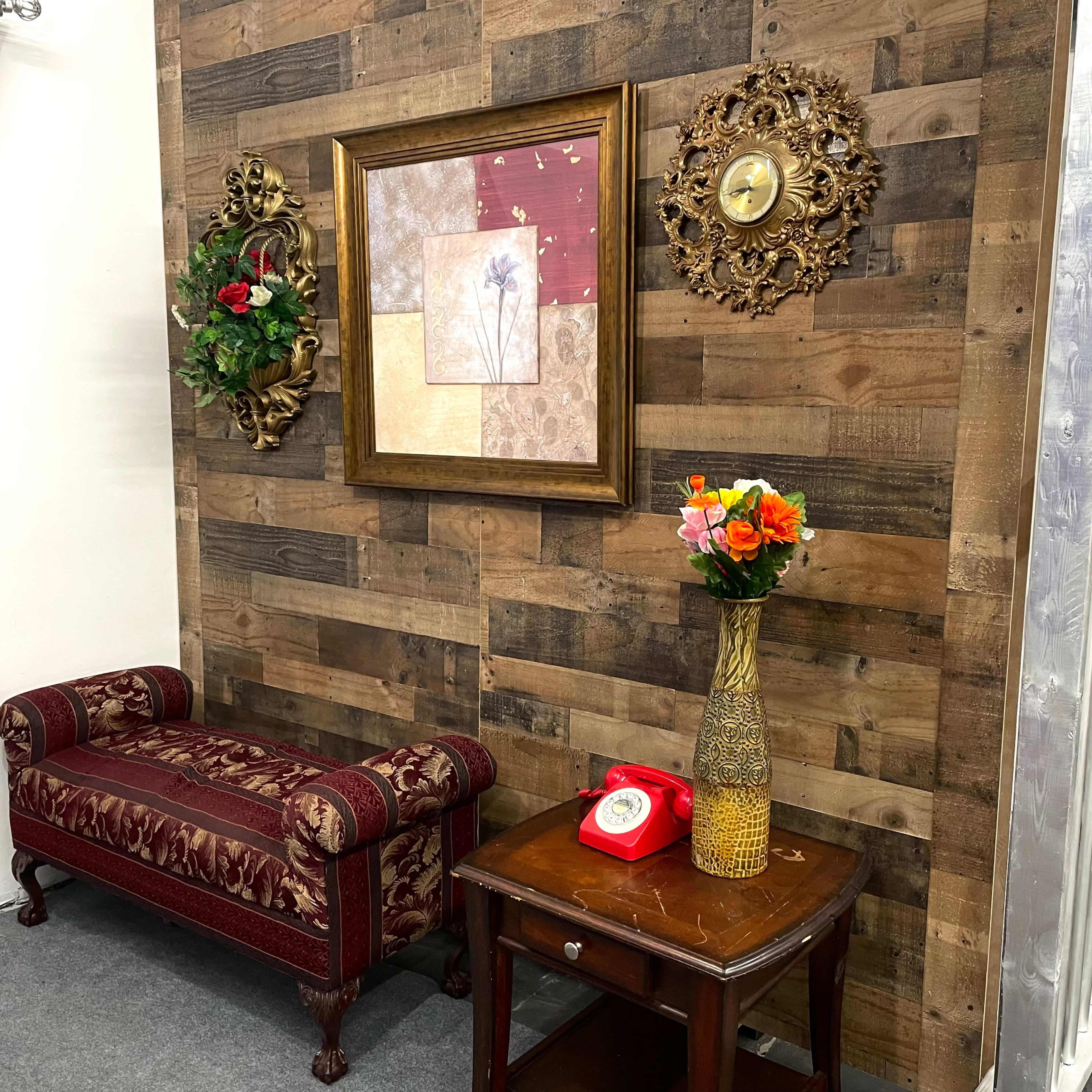 The scene features a small sitting area with a patterned sofa, a wooden table displaying a vase of flowers, and decorative wall art against a wood panel background.