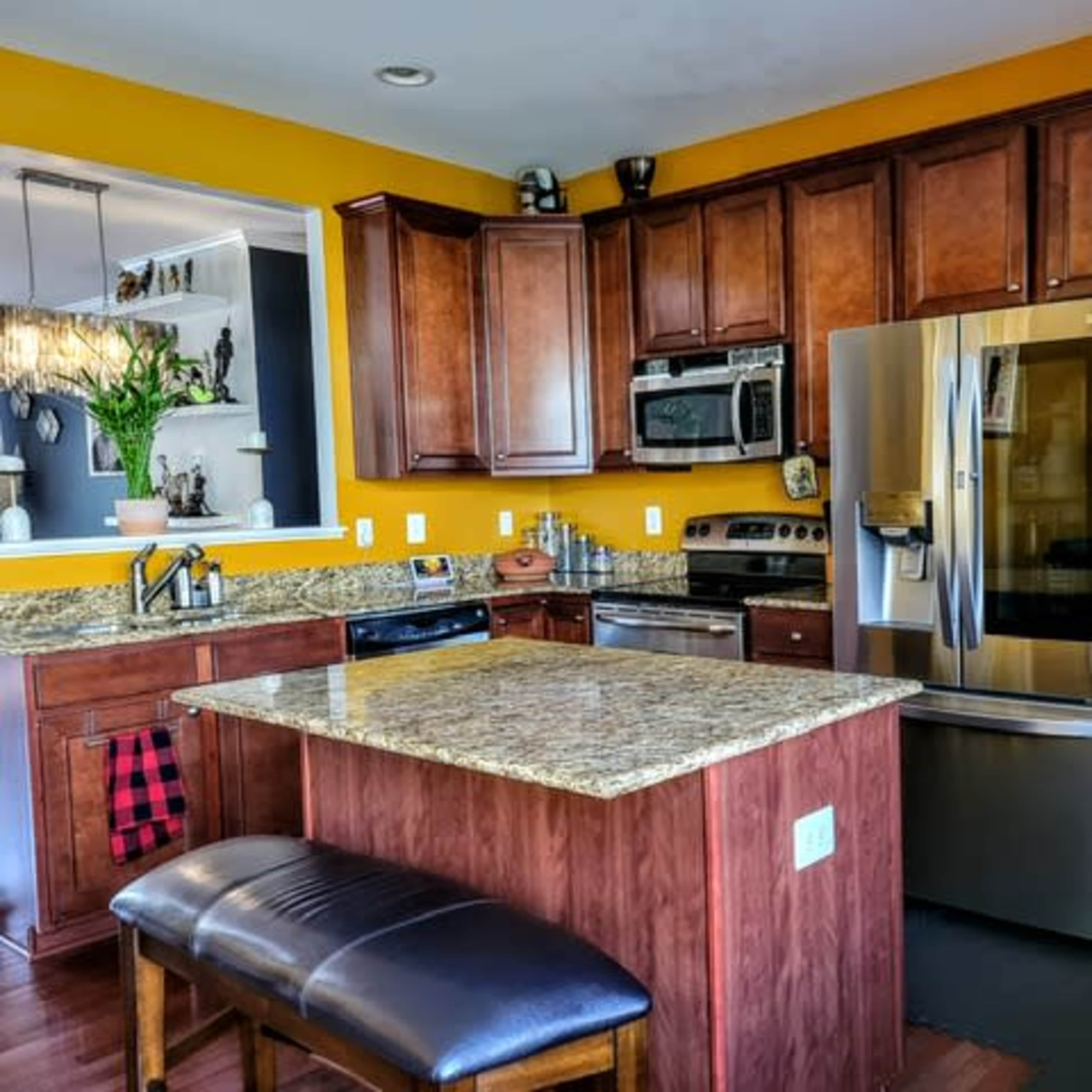 The kitchen features wooden cabinetry, a granite countertop island, stainless steel appliances, and yellow walls.