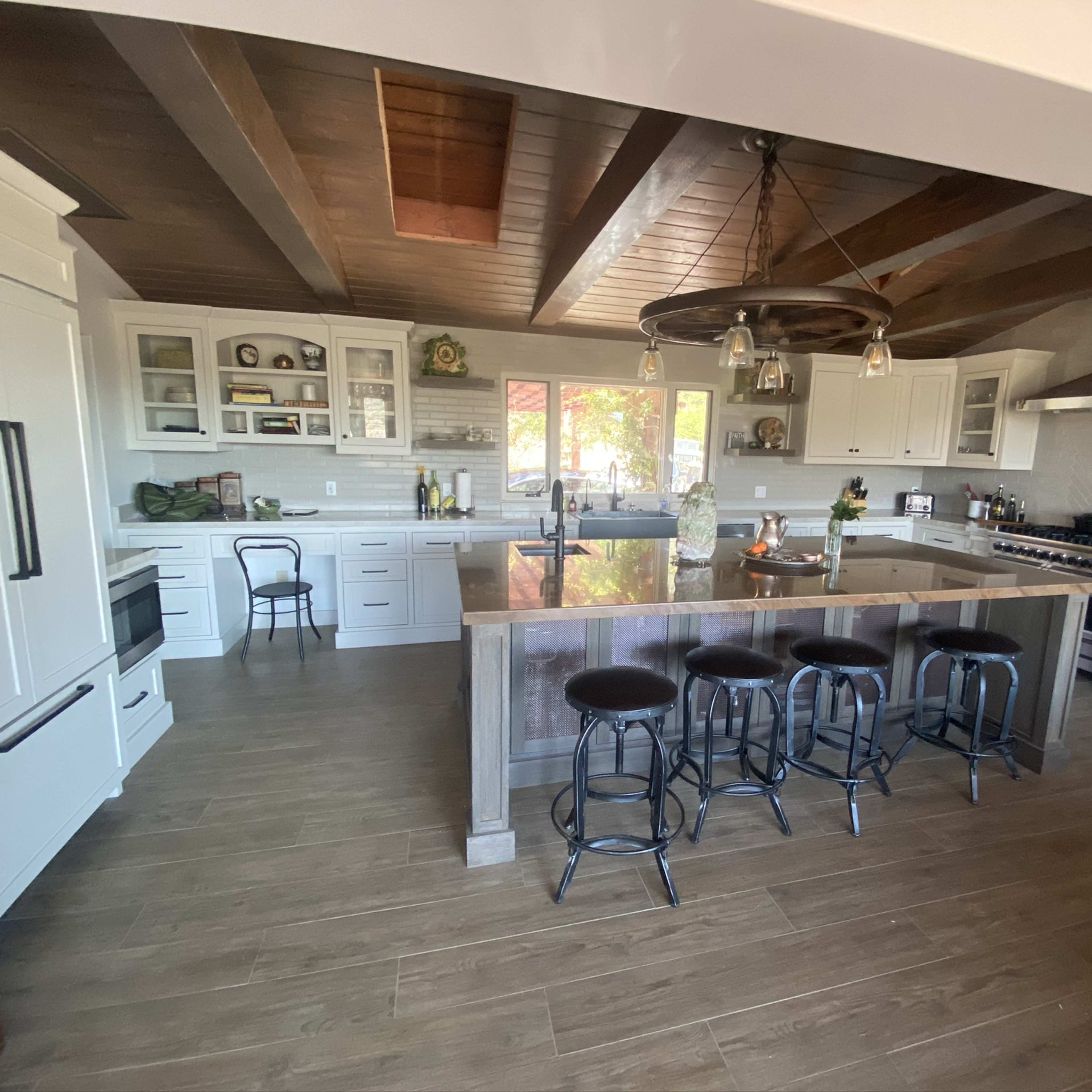 The kitchen features white cabinetry, a large central island with bar stools, and wooden beams on the ceiling.