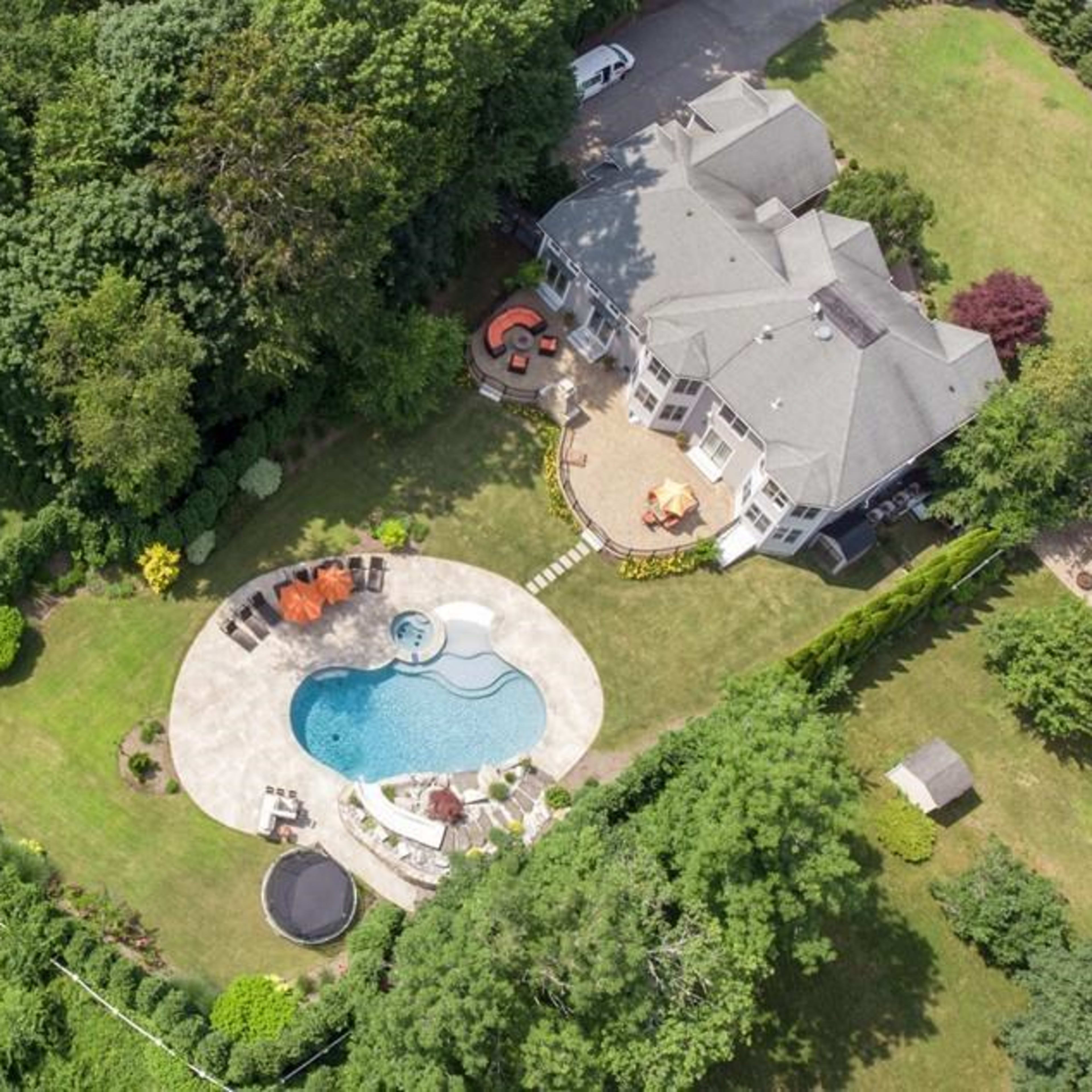 An aerial view of a large house with a swimming pool and landscaped yard surrounded by trees.