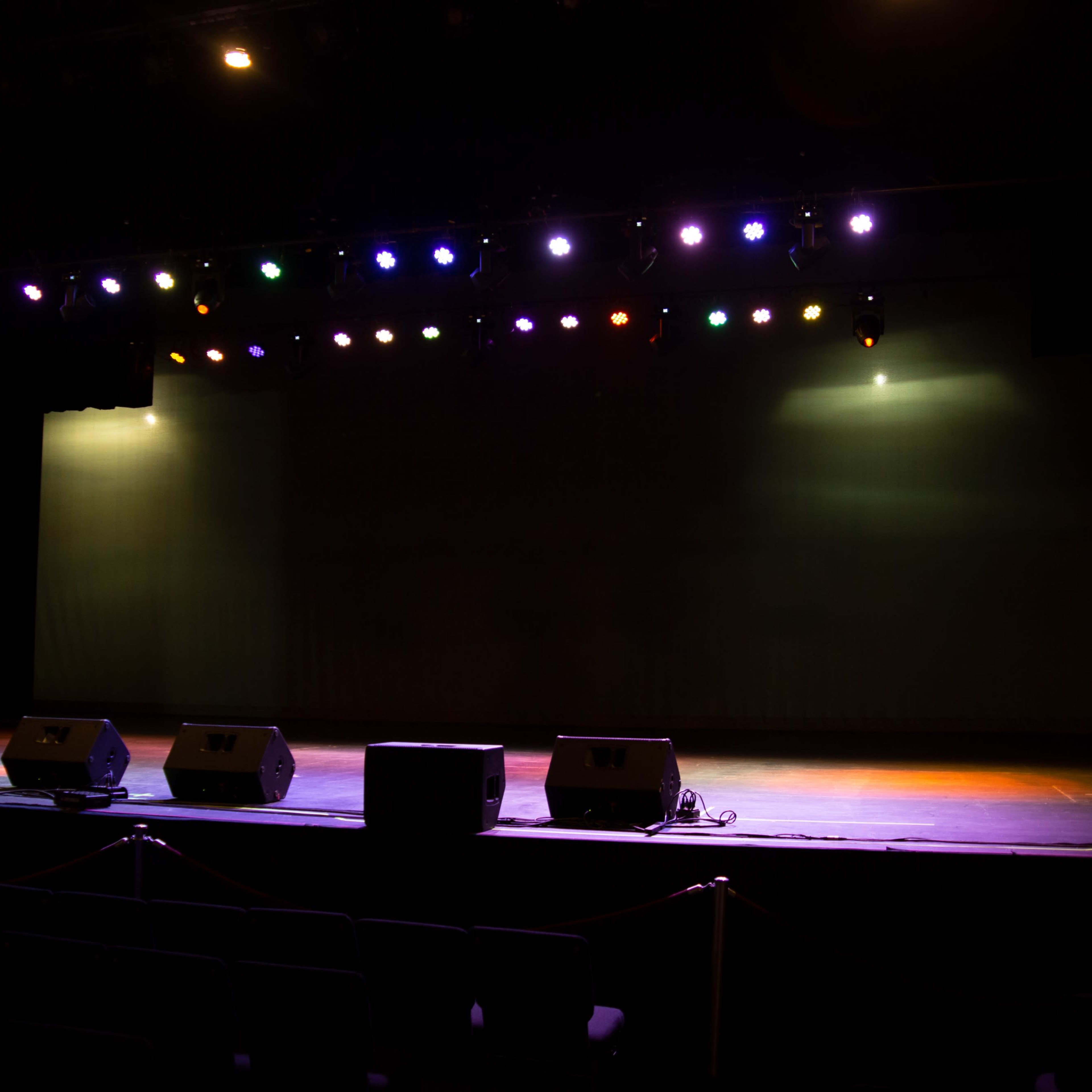 A dimly lit stage with colorful spotlights and sound equipment arranged in front.