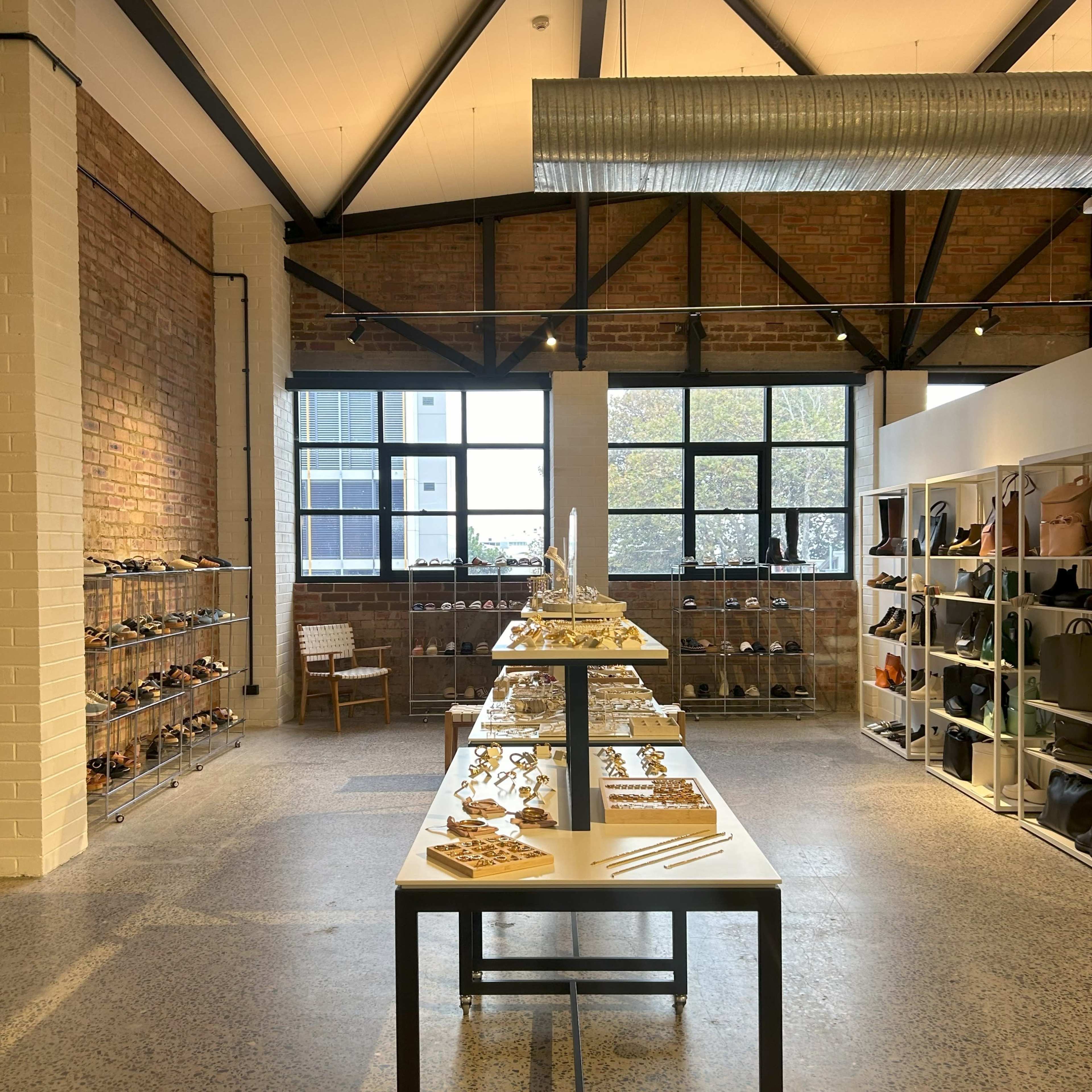 A retail store with a minimalist design, featuring shelves of shoes on one side and a table displaying accessories in the center, all within a brick-walled space.