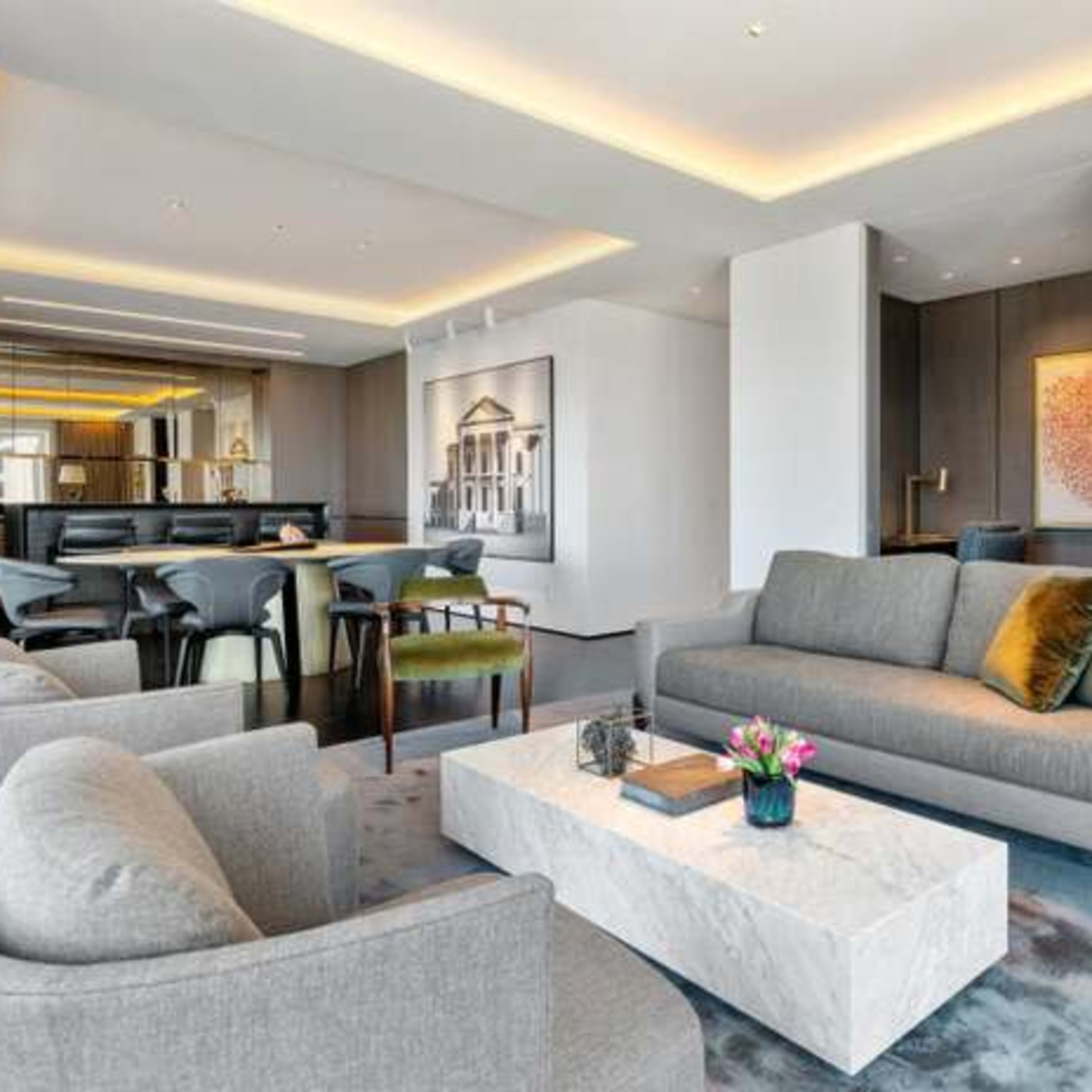 A modern living room with a gray sofa, a marble coffee table, and seating around a dining area in the background.