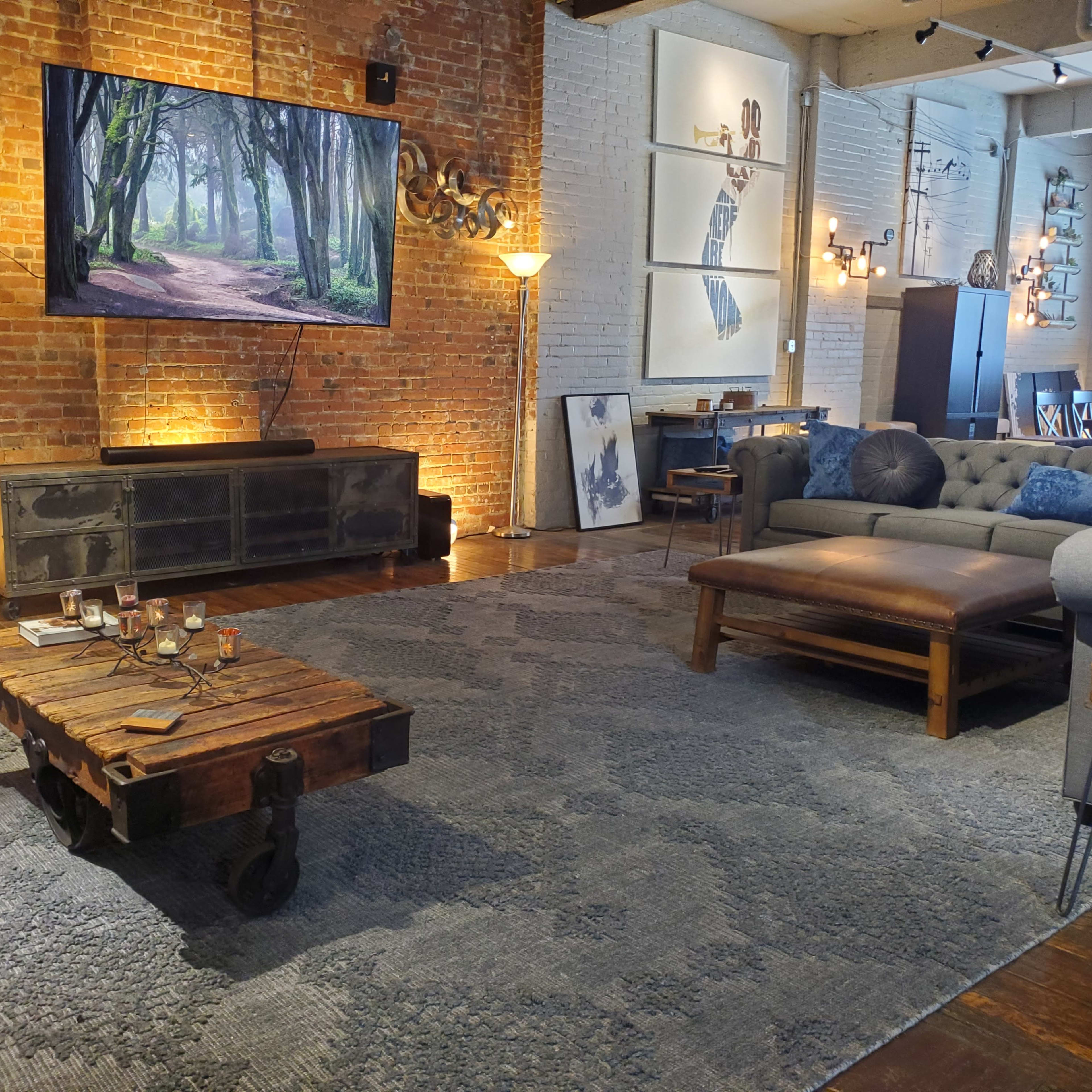 The living room features a large television mounted on a brick wall, with a wooden coffee table on a patterned rug and comfortable seating arranged around the space.