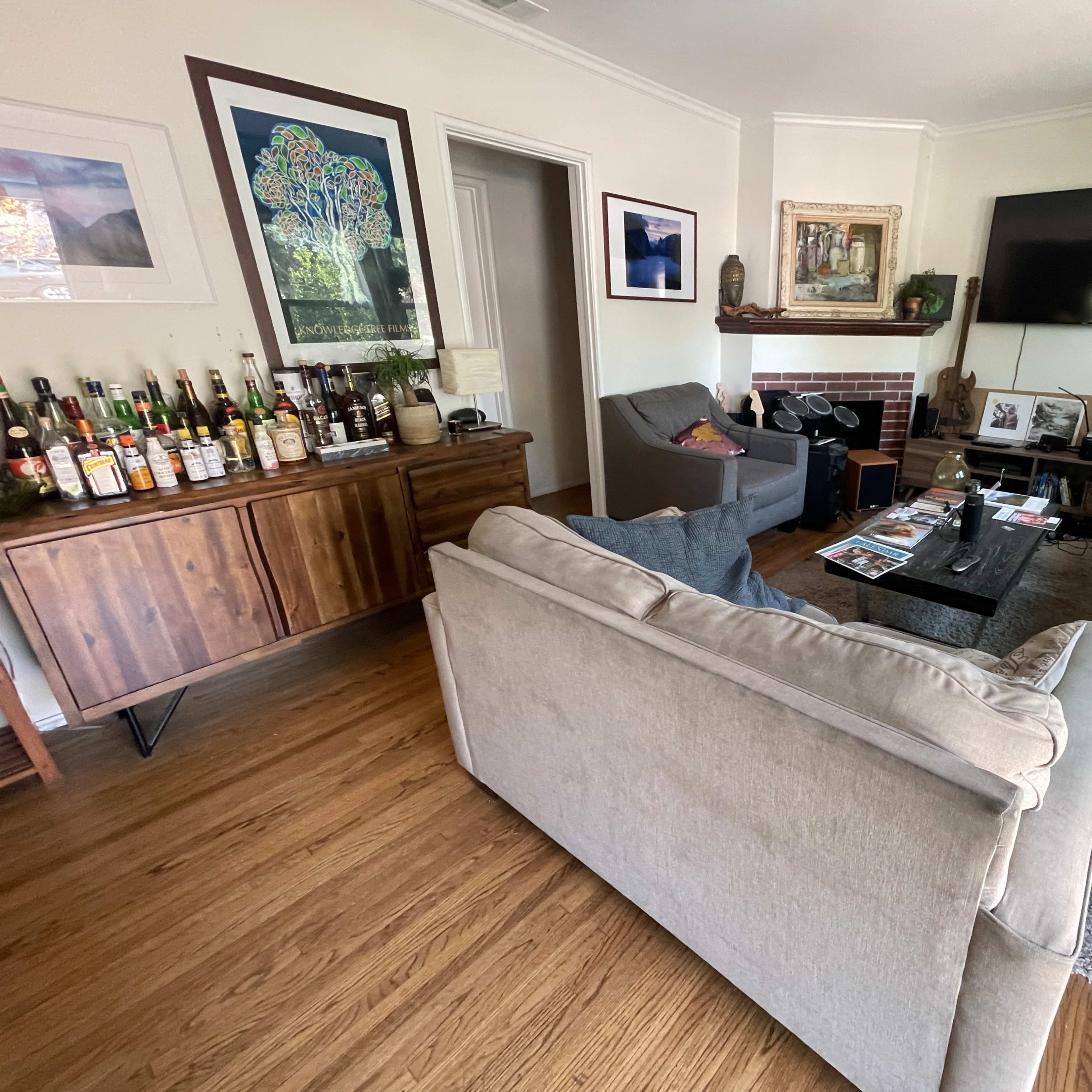 A cozy living room with a sofa, an armchair, a coffee table, and a wooden sideboard displaying various bottles.
