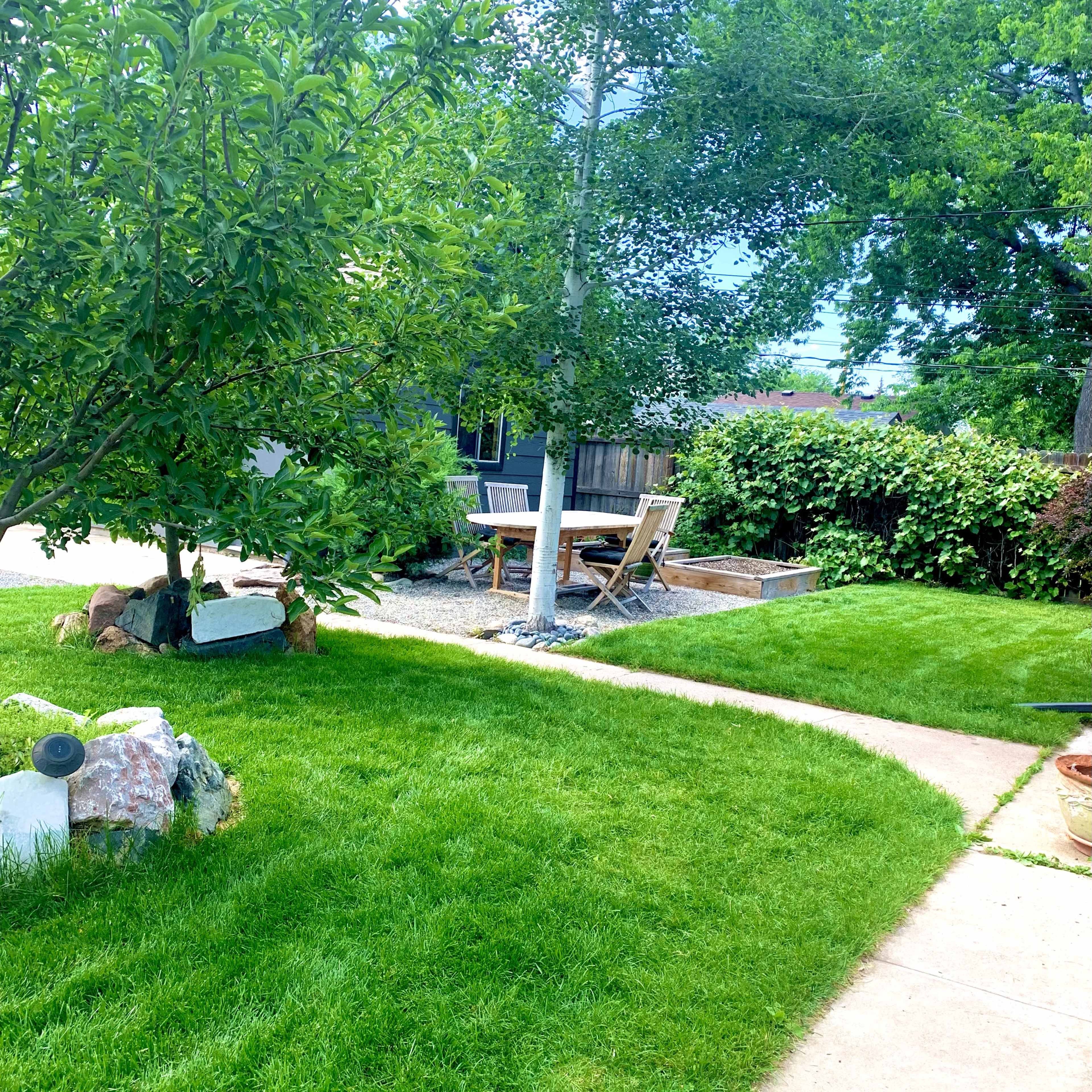 A well-maintained garden features a grassy area, a tree, a gravel path, and a wooden seating arrangement.