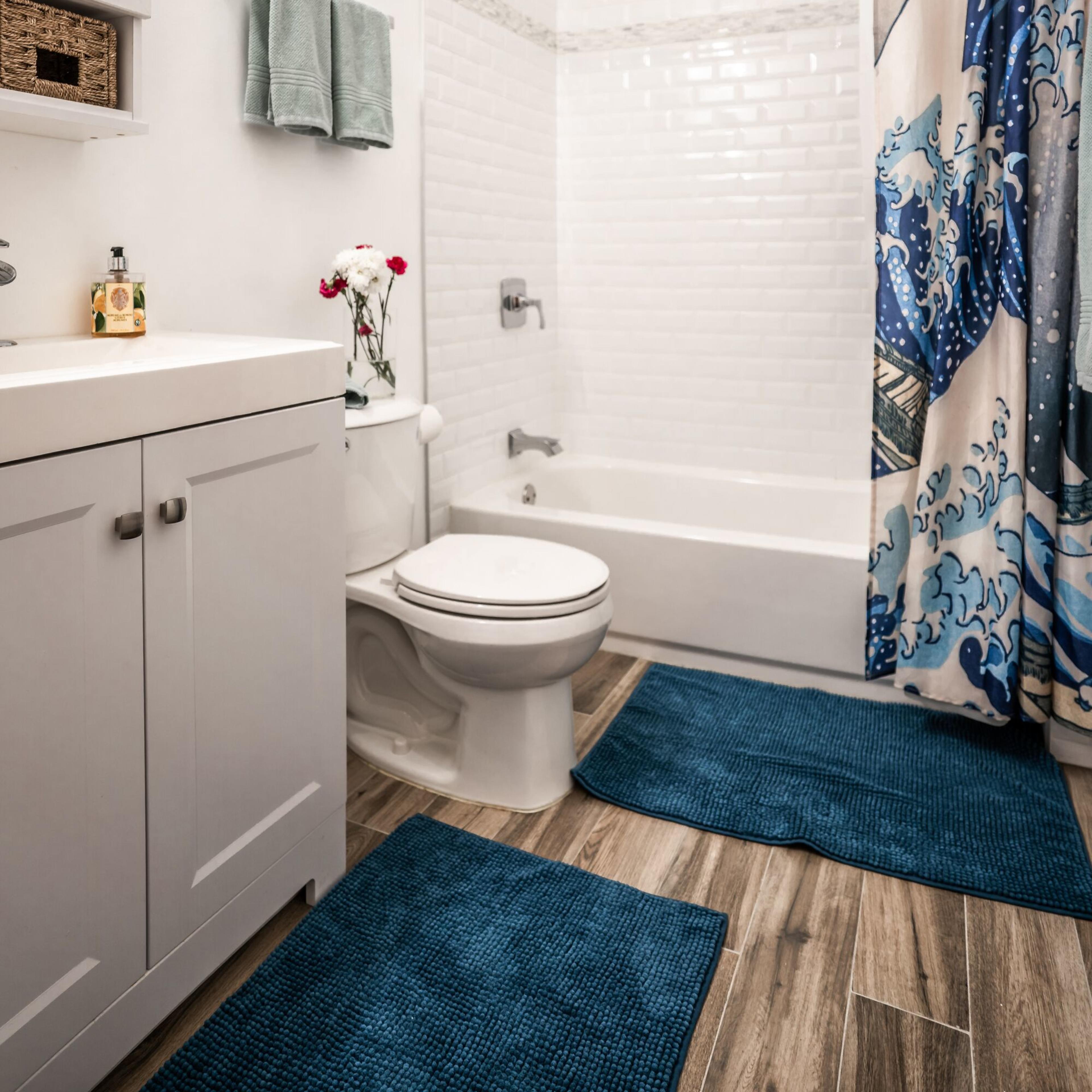 A modern bathroom features a shower with a glass door, a white bathtub, a vanity with storage, and colorful towels and a shower curtain with a wave design.