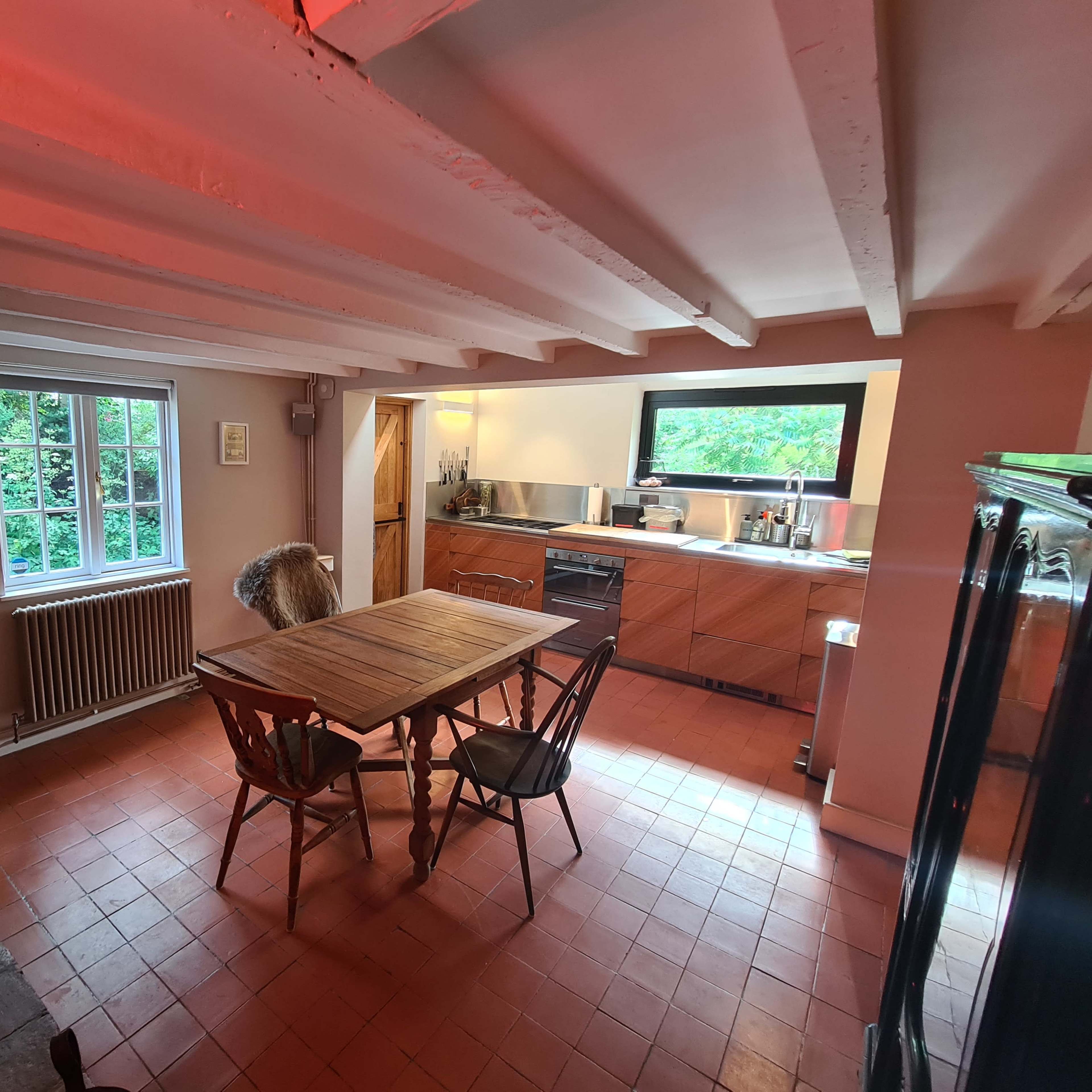 A kitchen with a wooden dining table and chairs, a window providing natural light, and modern appliances against a backdrop of rustic elements.