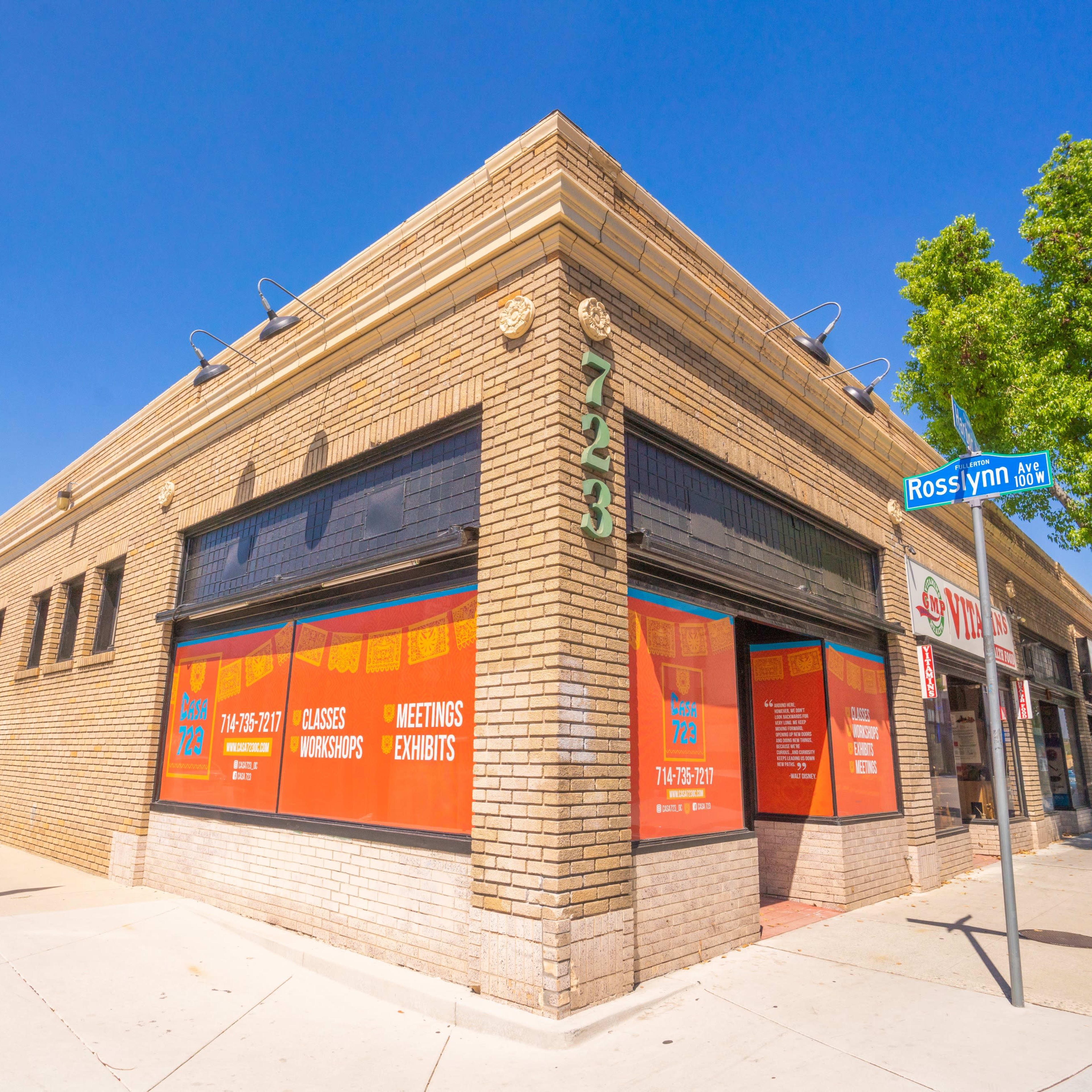 A brick building features large orange window signs advertising meetings and workshops, located at the corner of Rosslyn Street.