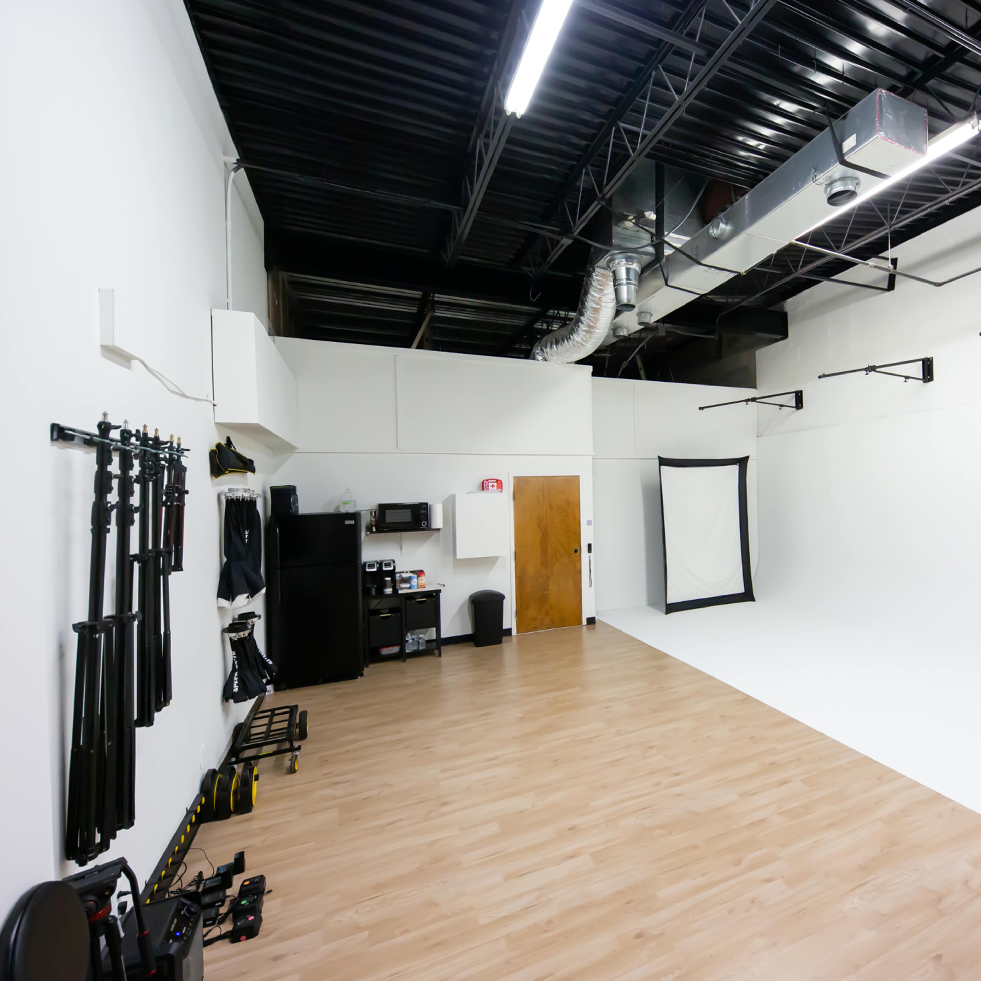 A spacious photography studio with white walls, a hardwood floor, and equipment along one side.