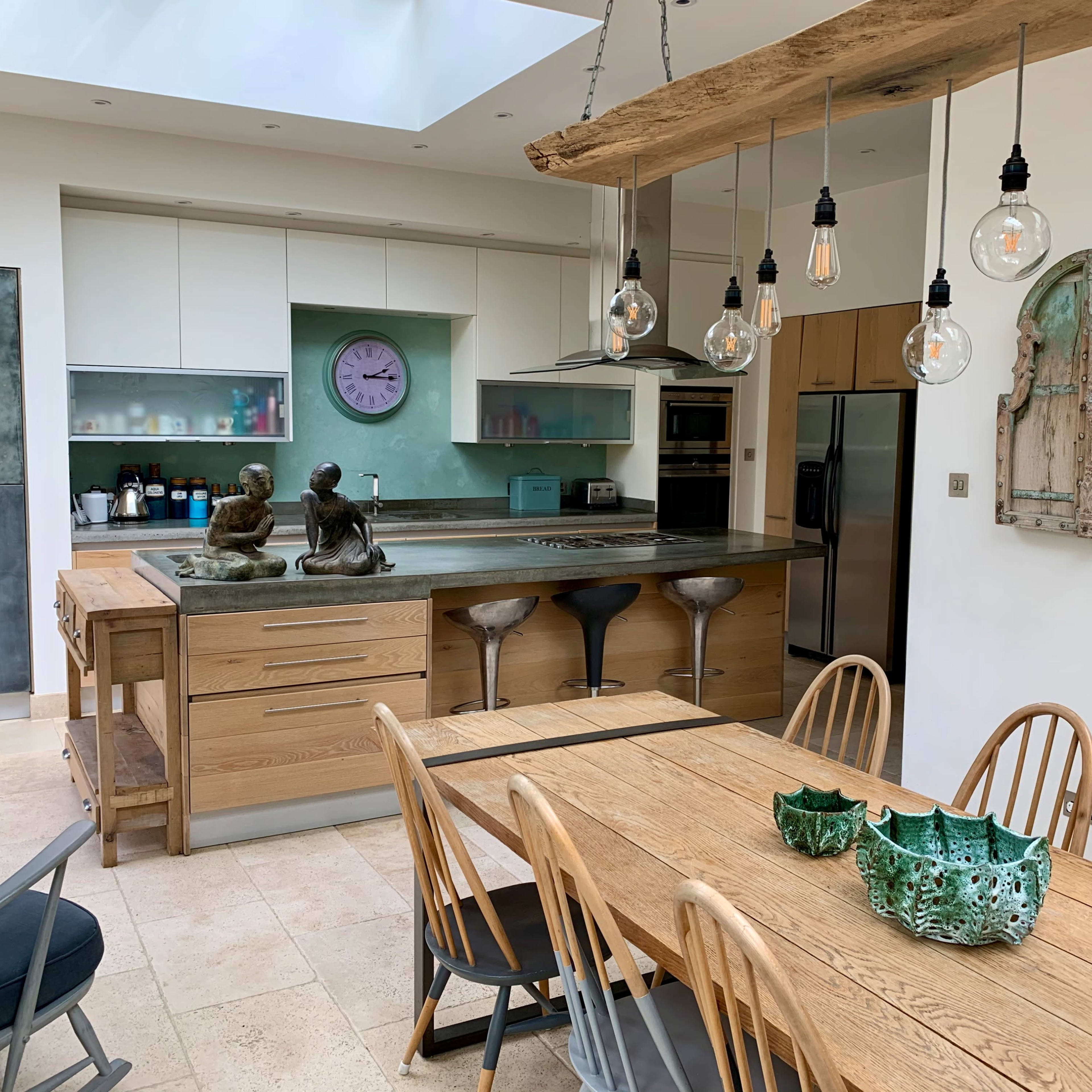 A modern kitchen with a large wooden dining table, stools at a kitchen island, and decorative elements including statues and unique light fixtures.