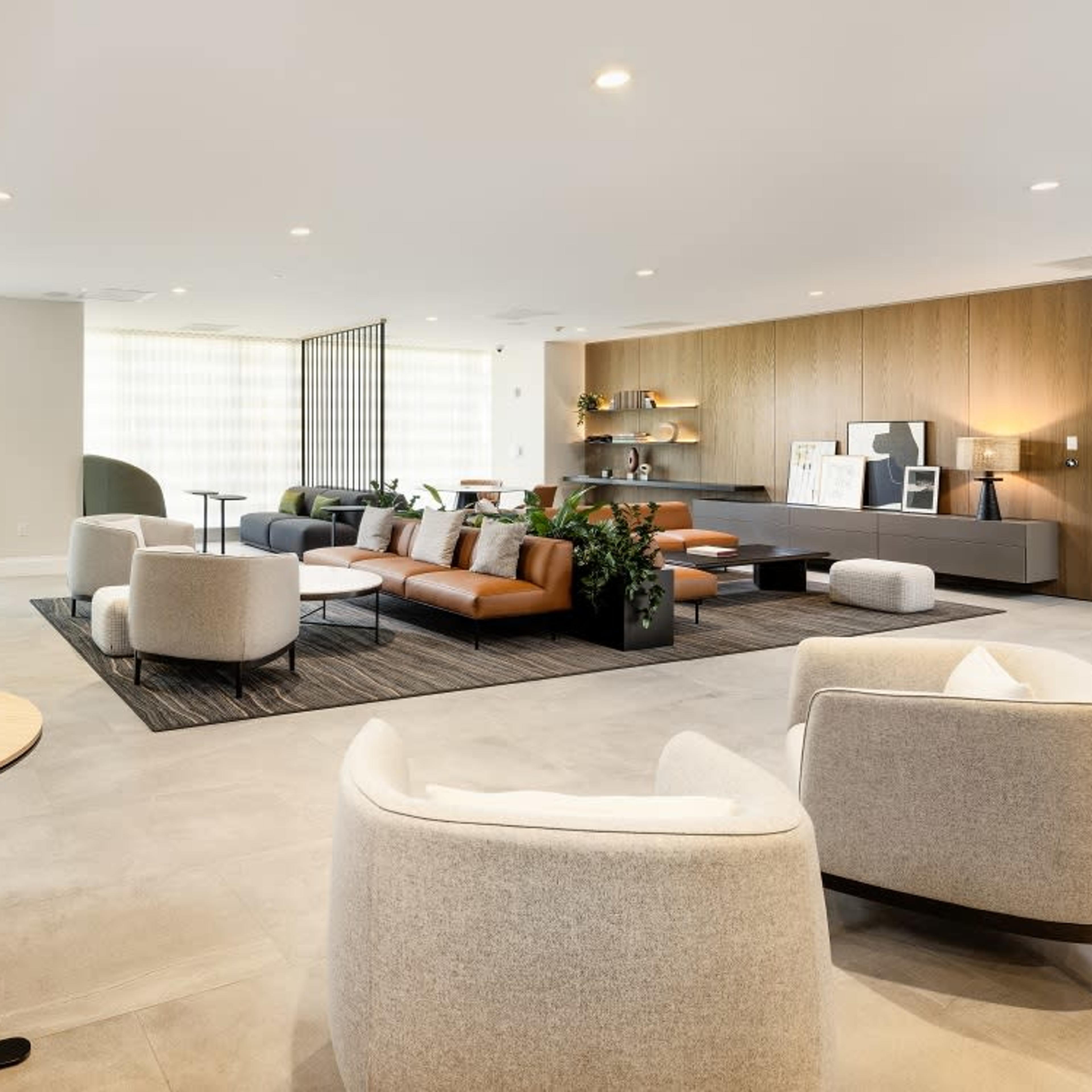 A modern lounge area featuring green and brown seating, small tables, and a variety of plants.