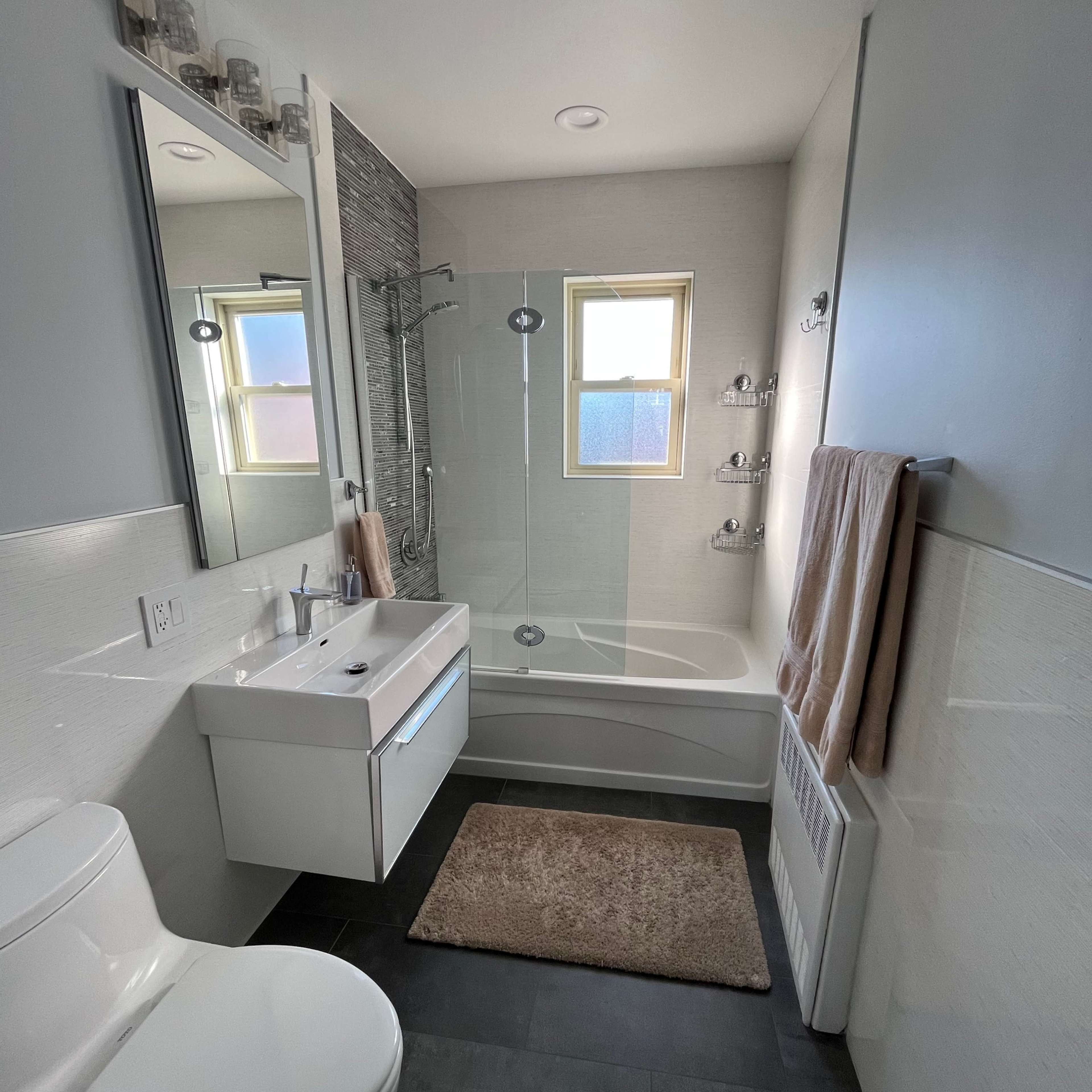 A modern bathroom featuring a glass shower, a bathtub, a white vanity with a mirror, and a toilet.