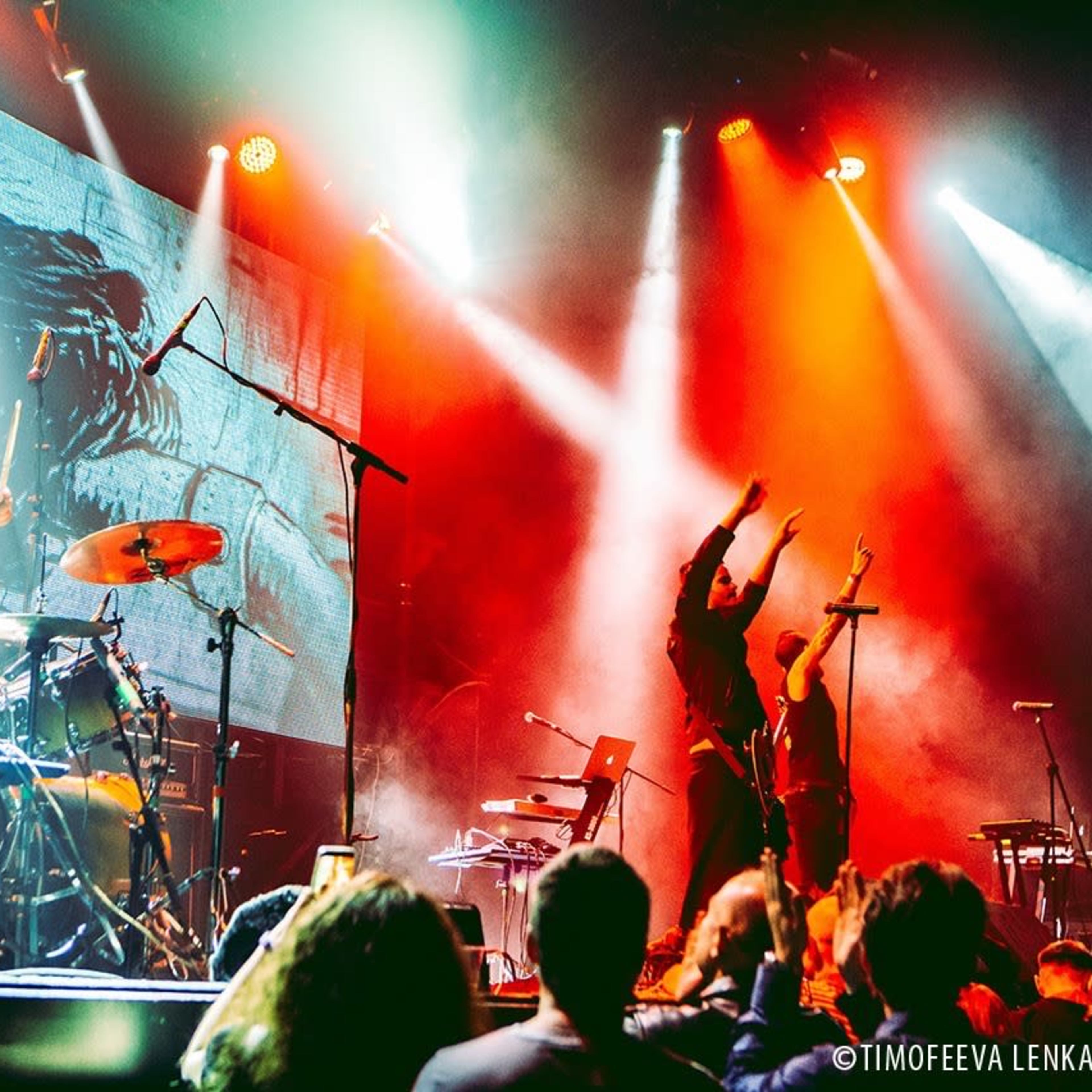 A band performs on stage with vibrant lights and an engaged audience.