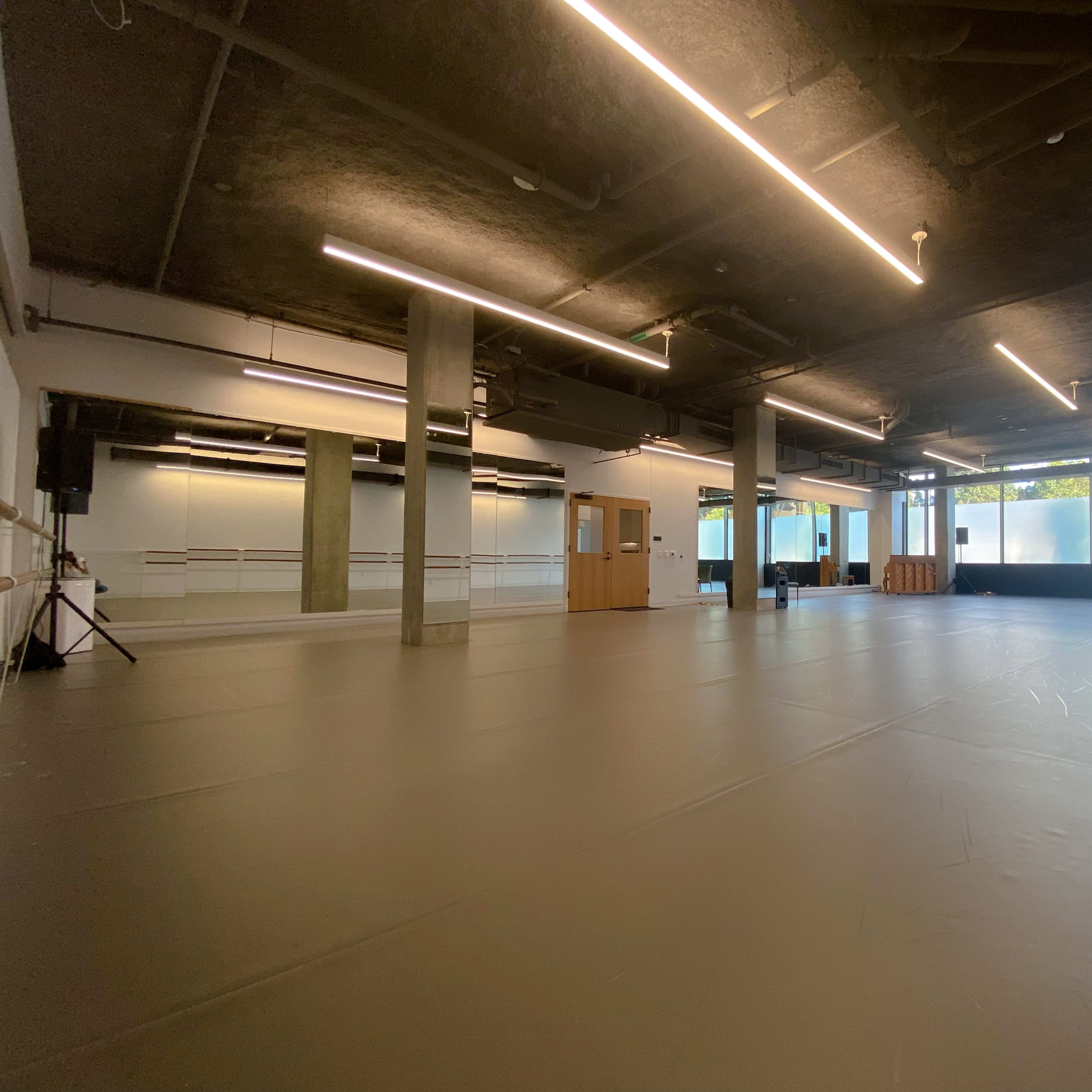 A spacious dance studio with a polished floor, large windows, and bright overhead lighting.