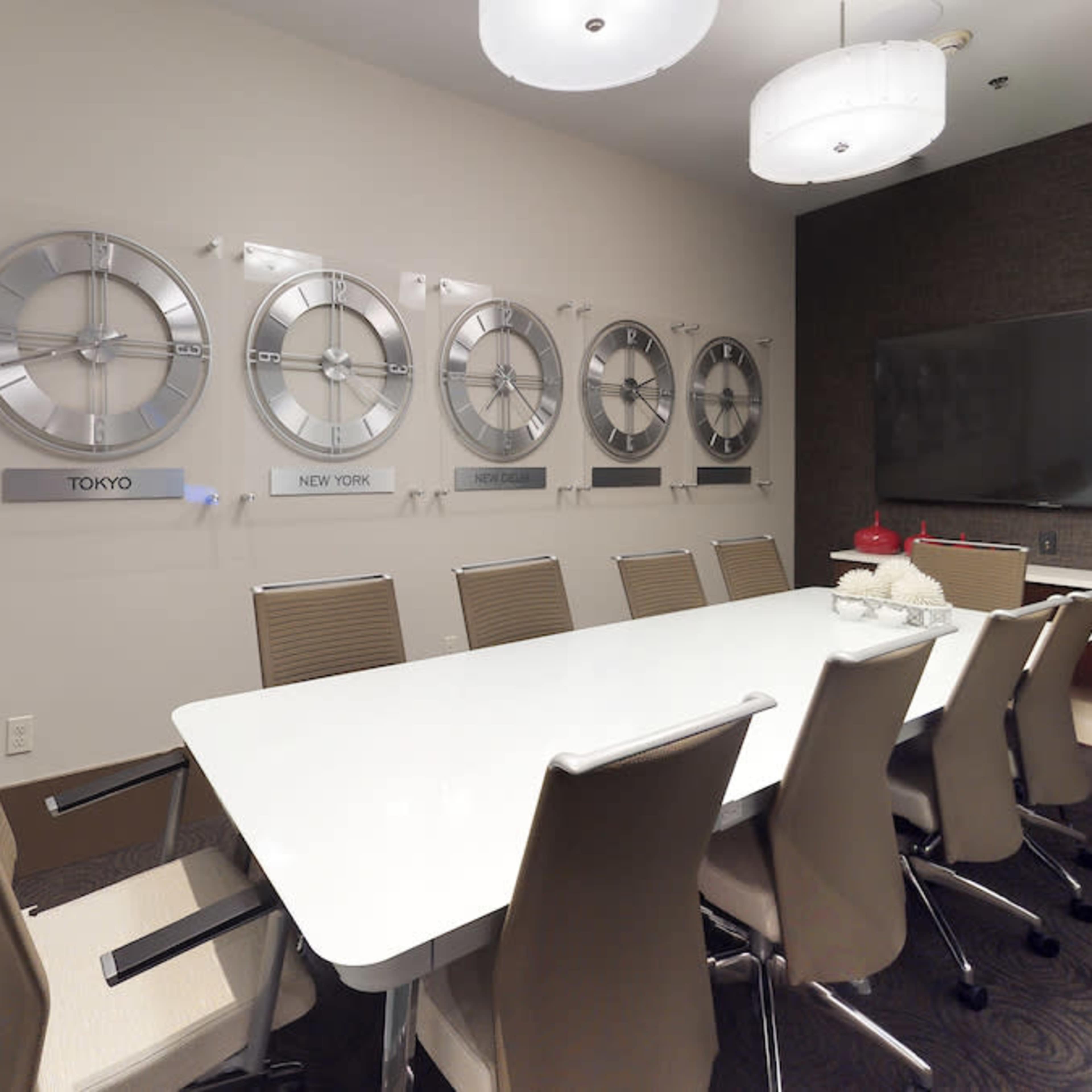A modern conference room features a long white table surrounded by chairs, with a wall displaying clocks for different time zones including Tokyo and New York.