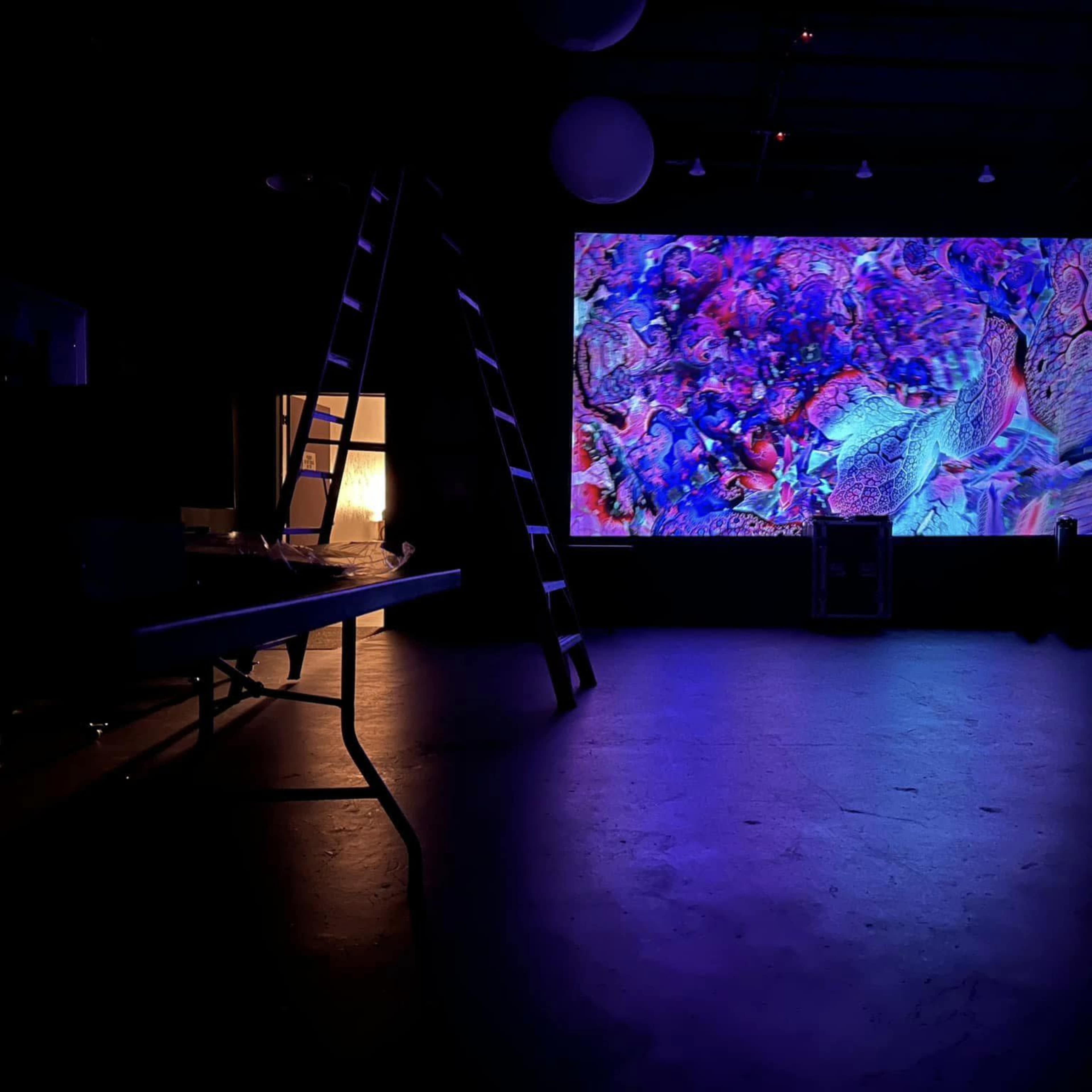 A large, colorful abstract projection on a wall in a dimly lit room, with a ladder and tables visible in the foreground.