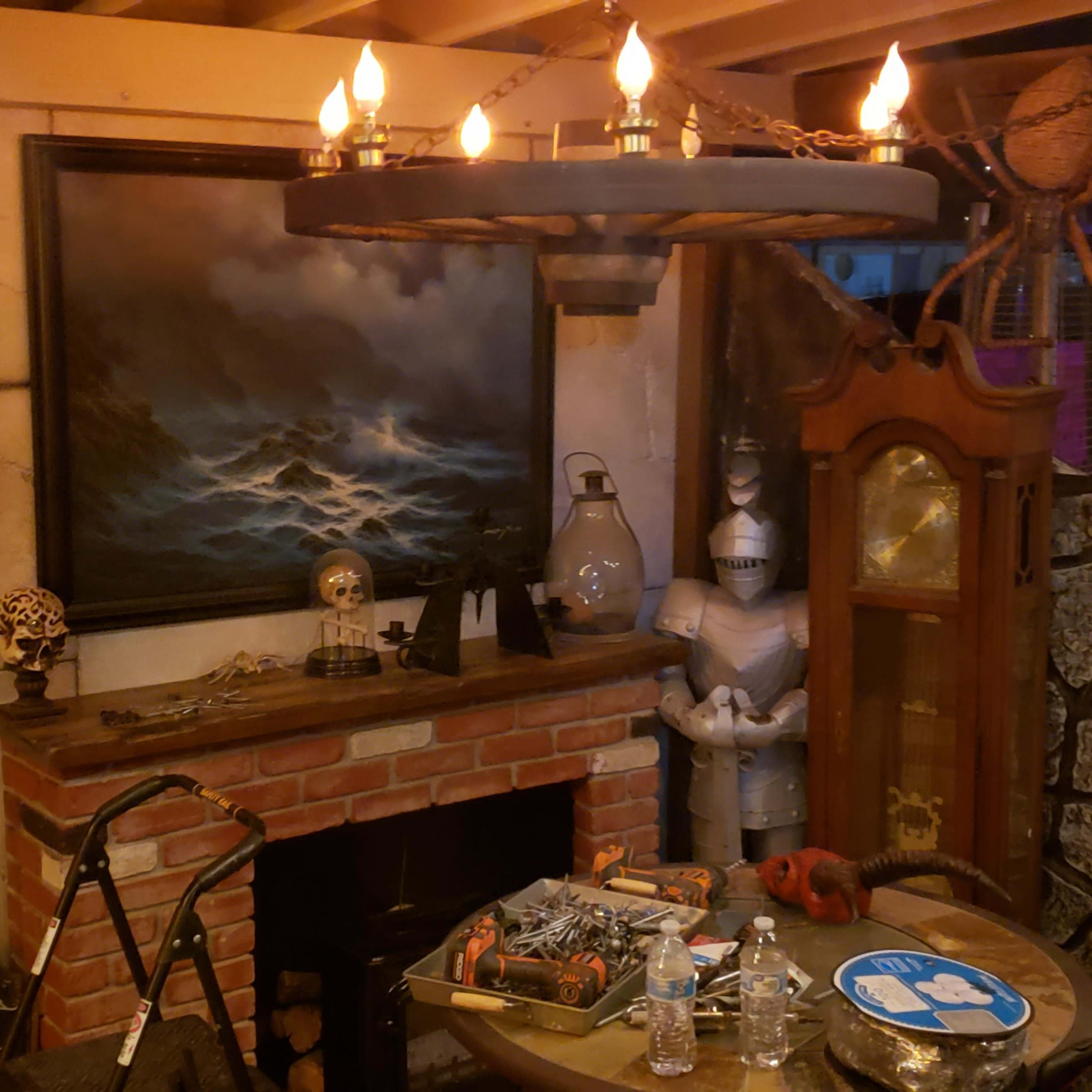 A rustic room with a brick fireplace, a chandelier with candles hanging above a table, and various nautical and historical decorations on the walls.