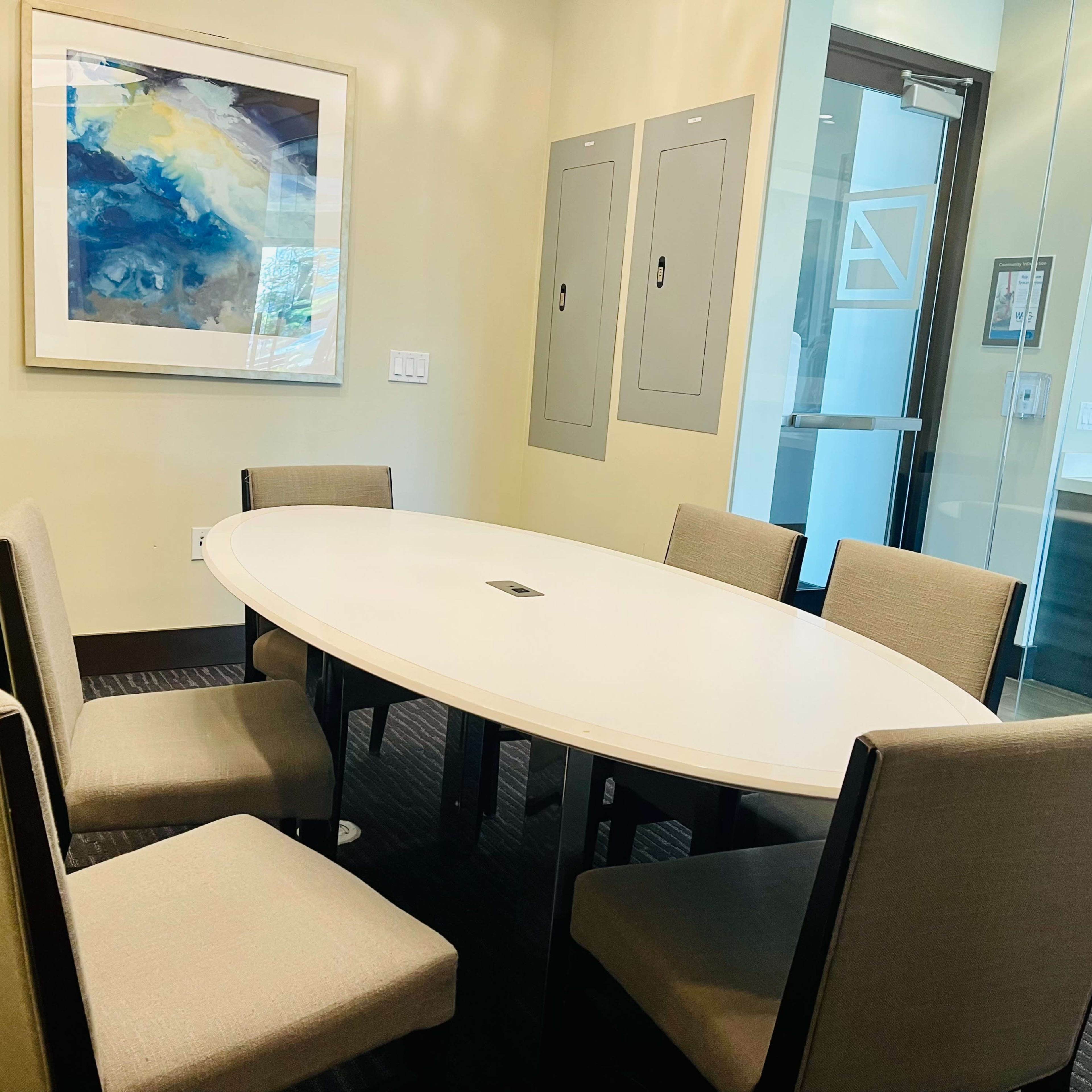 A round table surrounded by six beige chairs is situated in a well-lit conference room, accompanied by artworks on the walls.