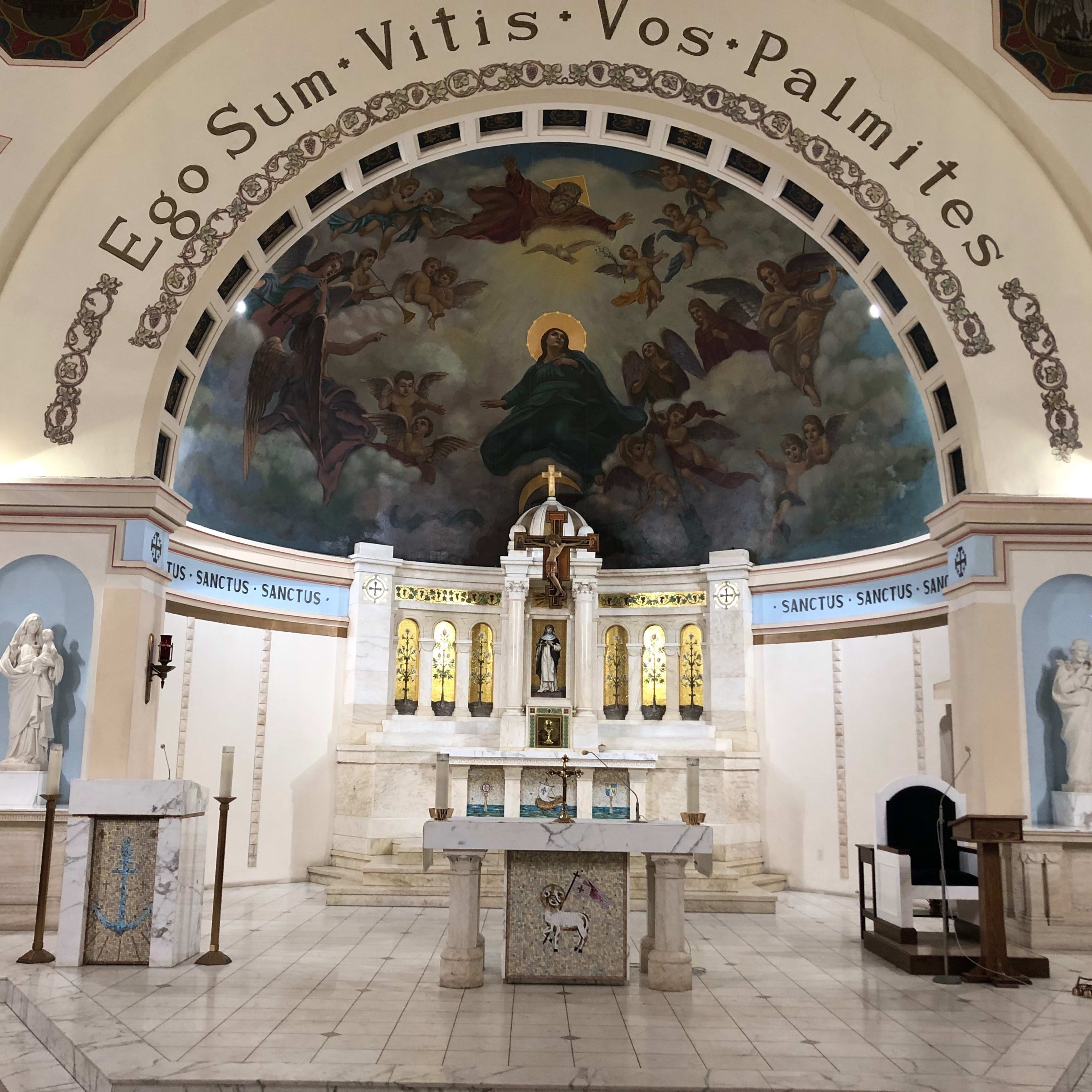 The interior of a church featuring an ornate altar with a large mural above it, surrounded by statues and decorative elements.