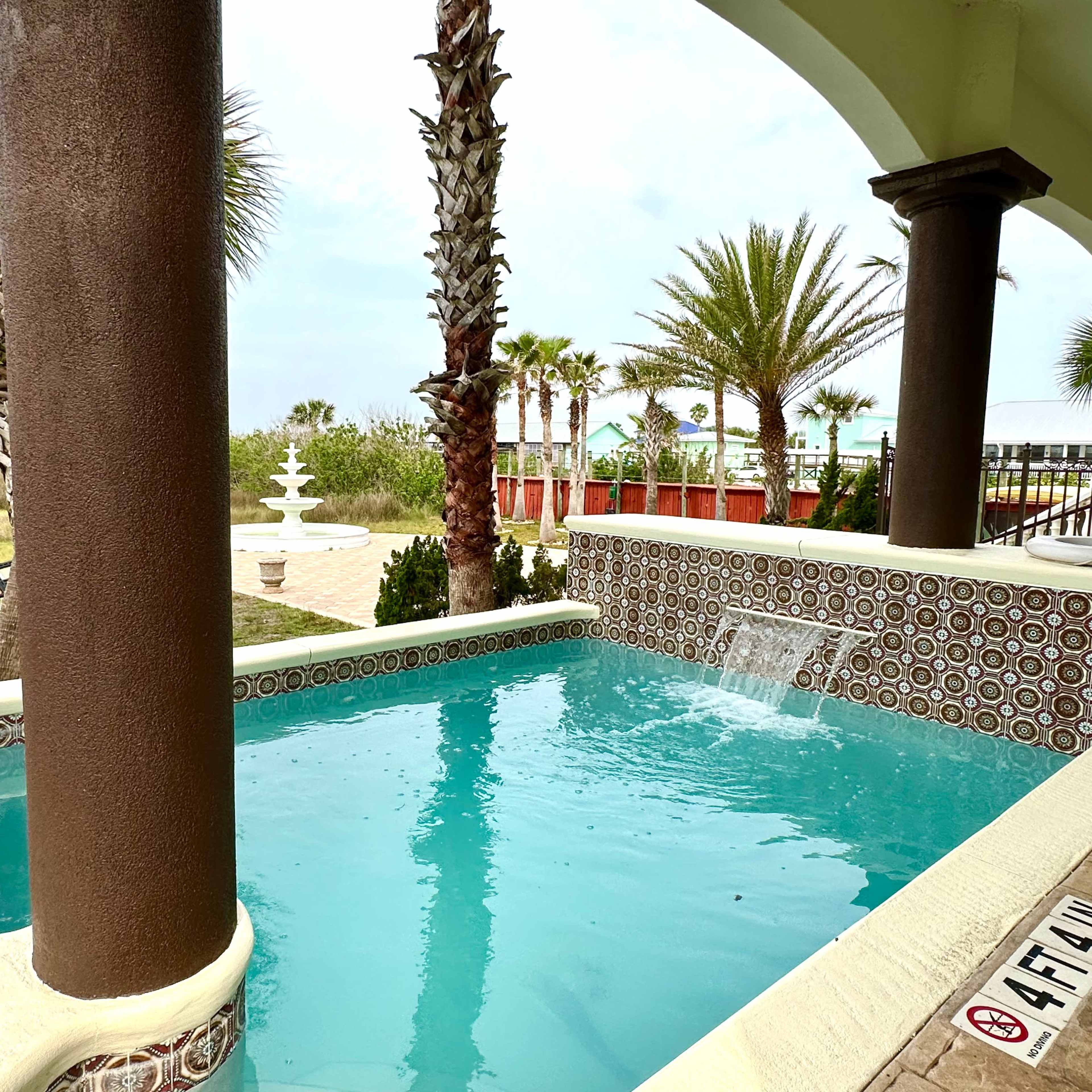 A small swimming pool surrounded by palm trees and a landscaped area.