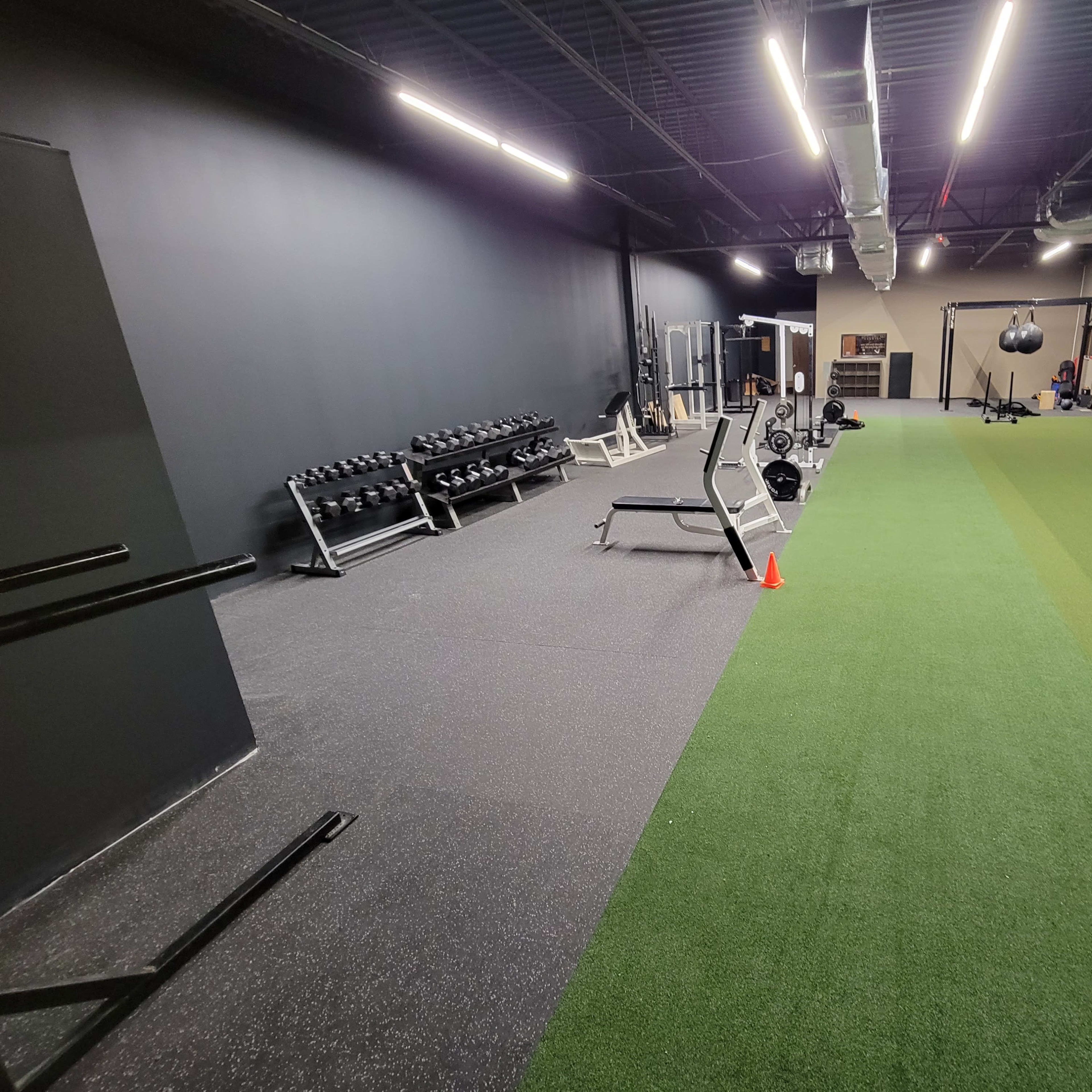 A gym interior with free weights and exercise equipment on one side, and a turf area for training on the other.