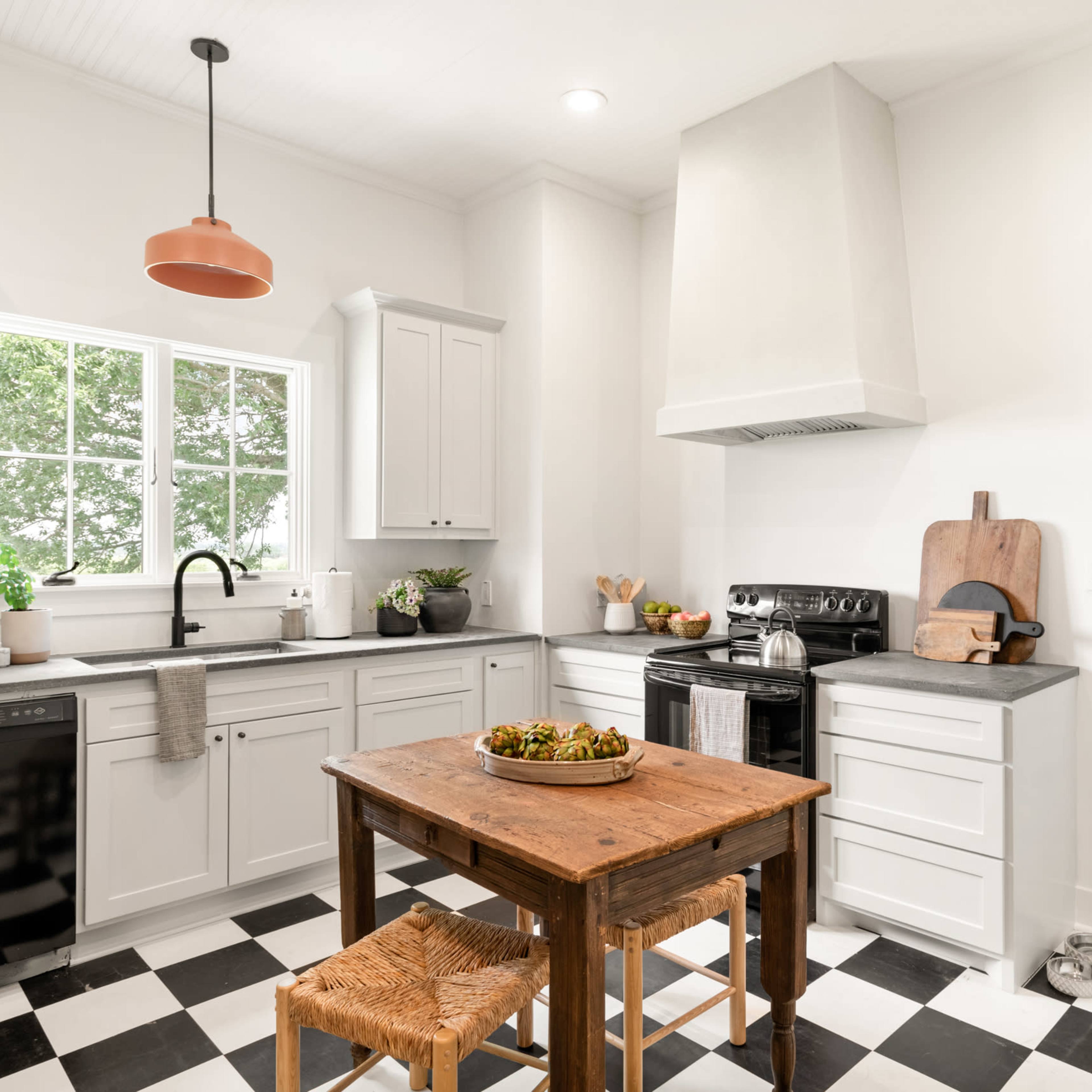 A modern kitchen with gray cabinetry, a black and white checkered floor, and a wooden table at the center.