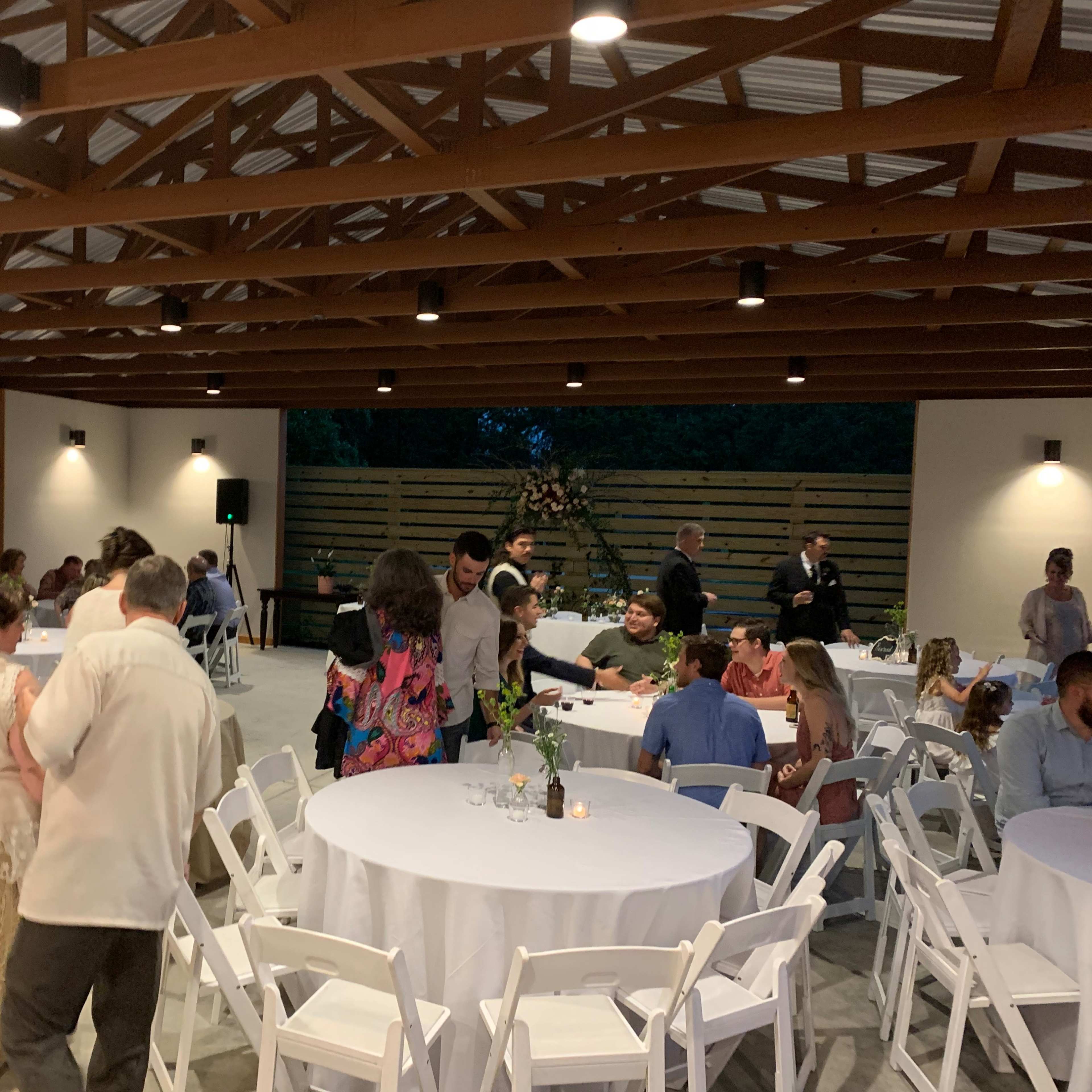 A spacious event space with round tables set for dining, where people are mingling and enjoying the evening.