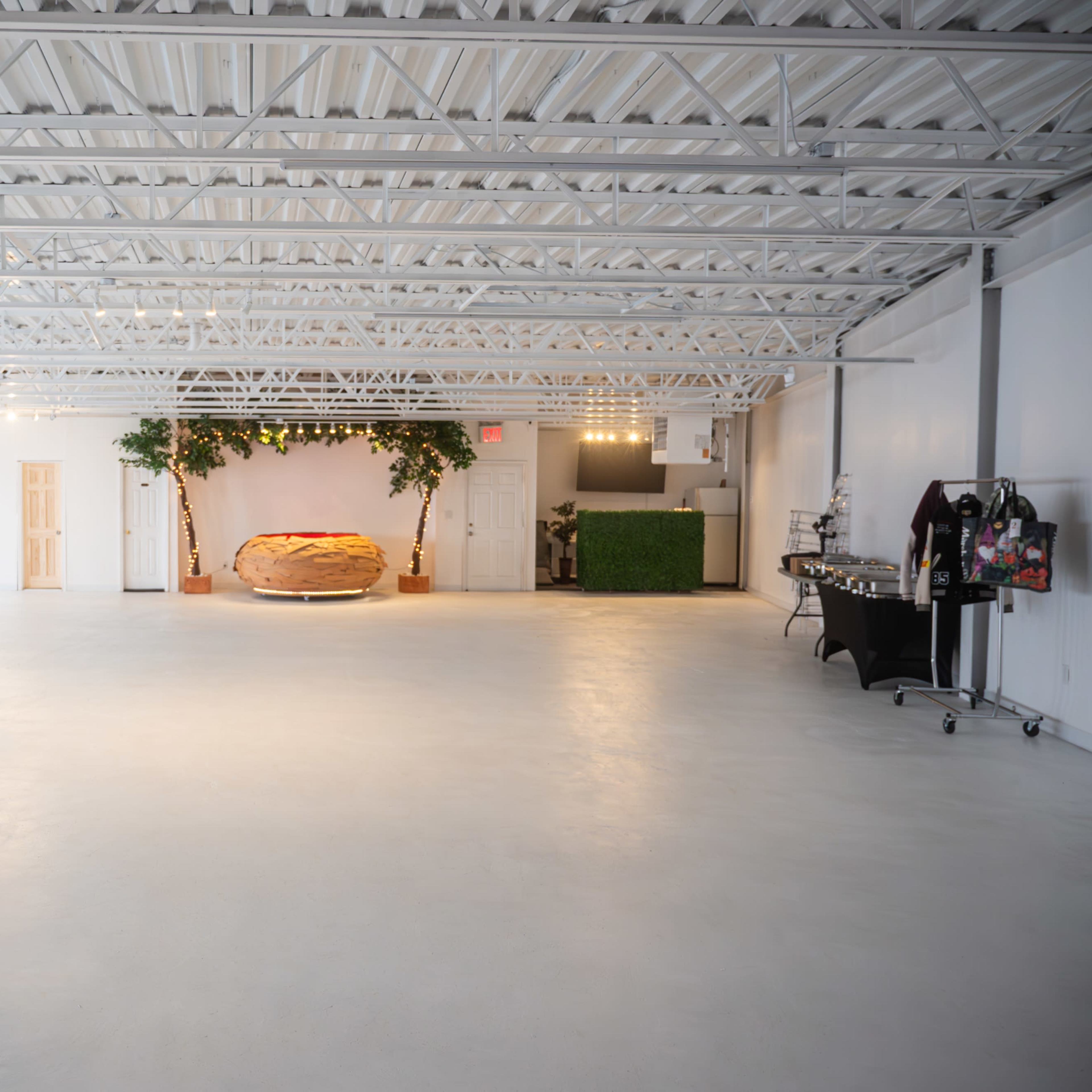 The spacious room features a circular seating area surrounded by greenery, with a refreshment table to the side.