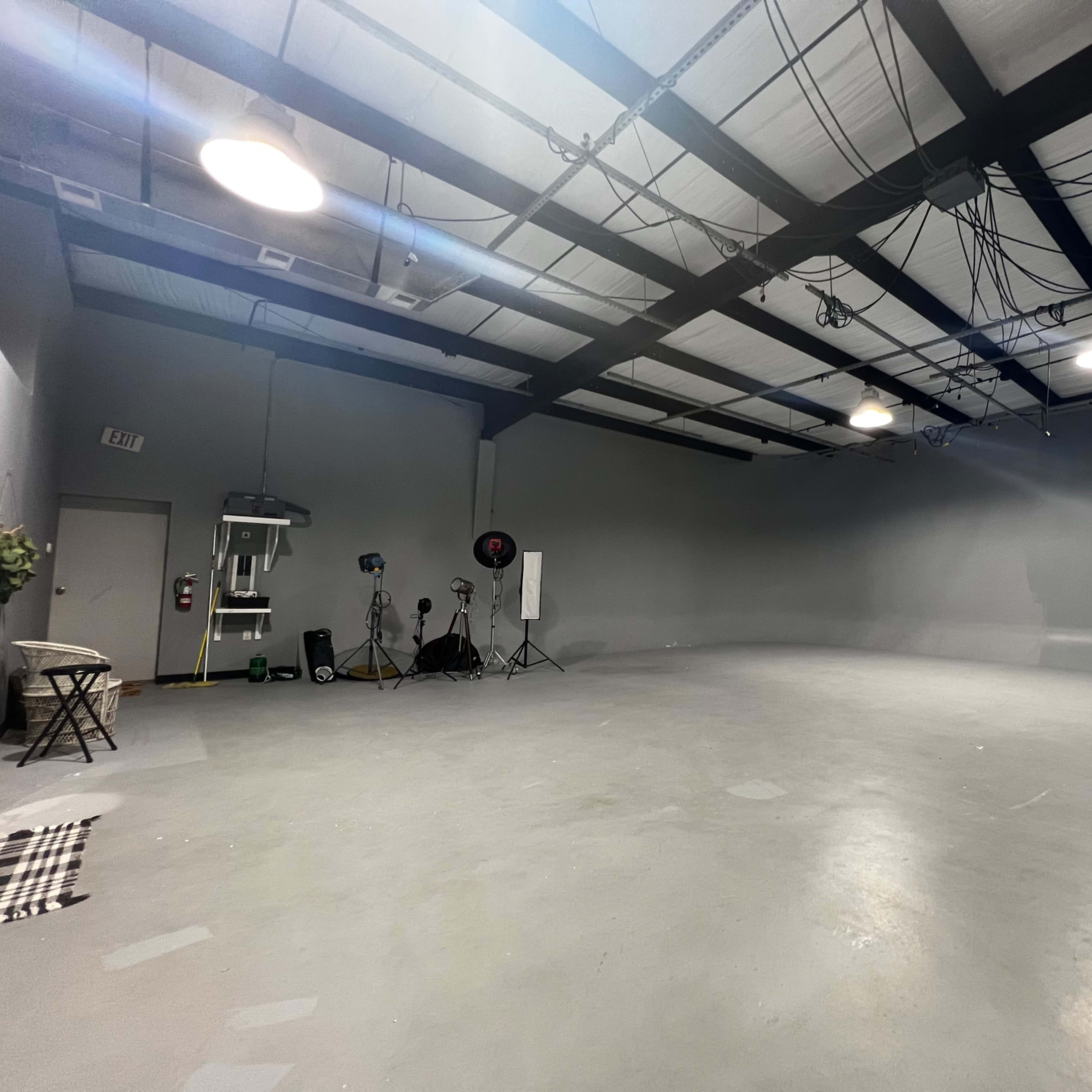 A spacious, empty interior room with gray walls, overhead lighting, and scattered photo equipment.