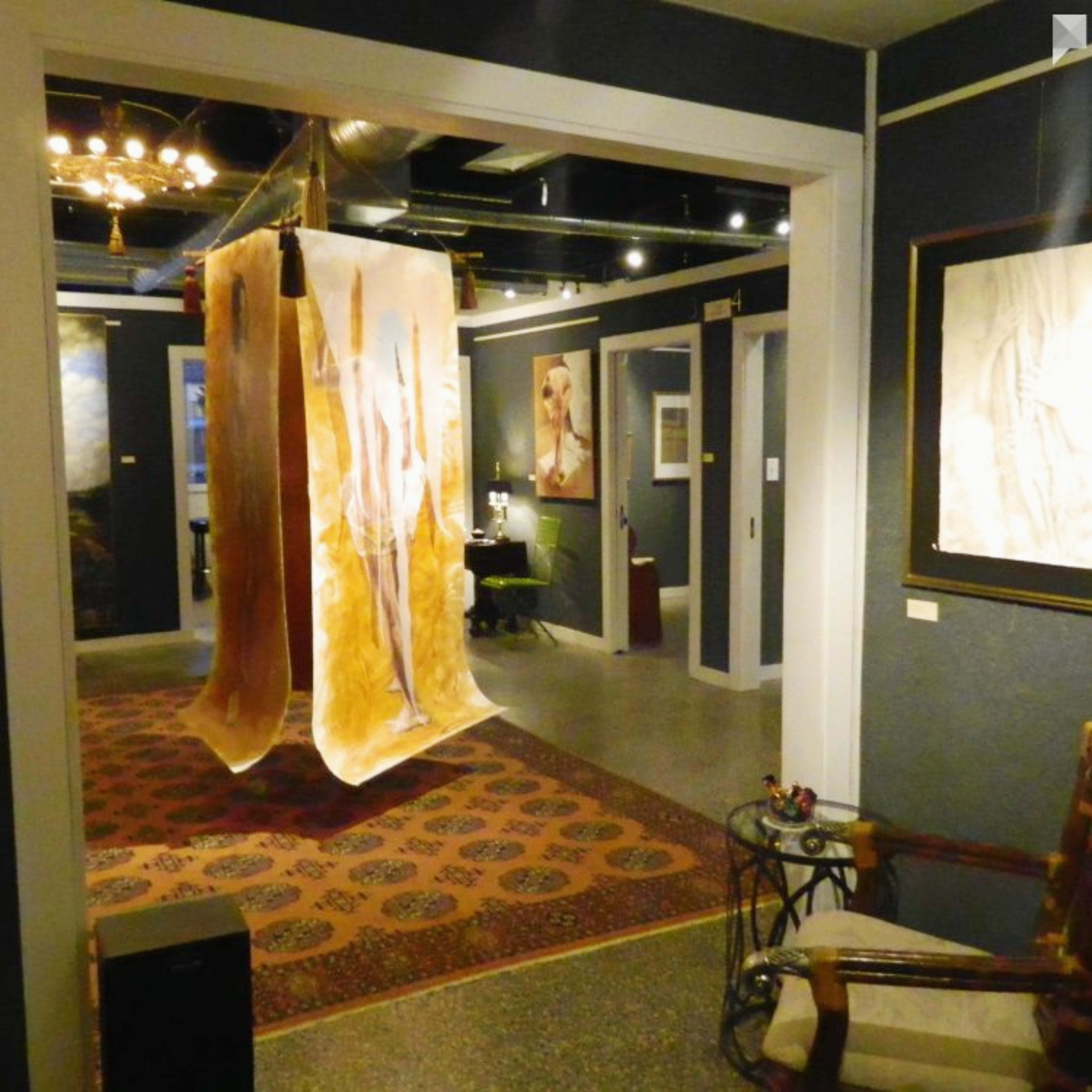 An art gallery interior with a hanging fabric installation and various artworks displayed on the walls.