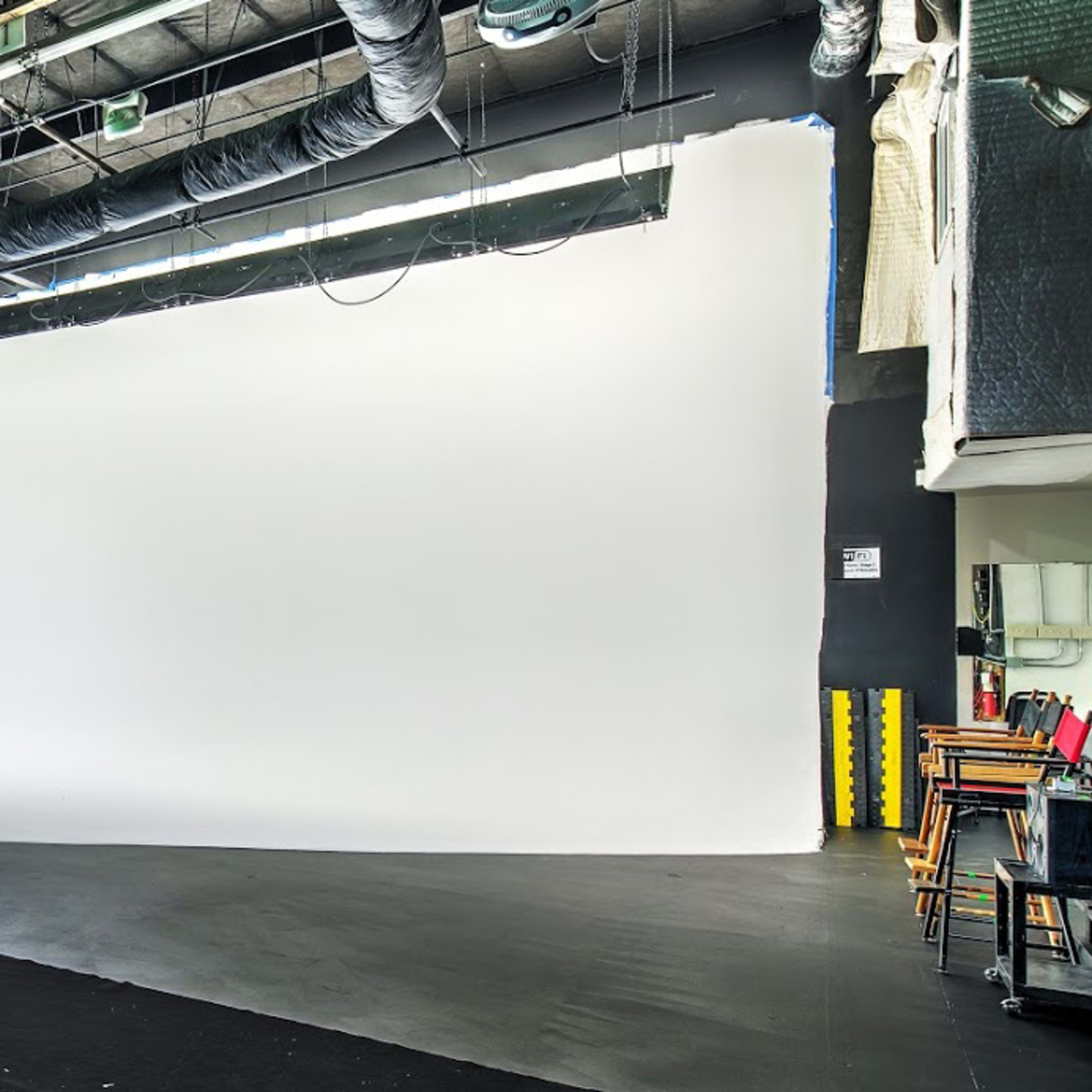 A spacious photography studio with a large white backdrop and studio lights mounted on the ceiling.