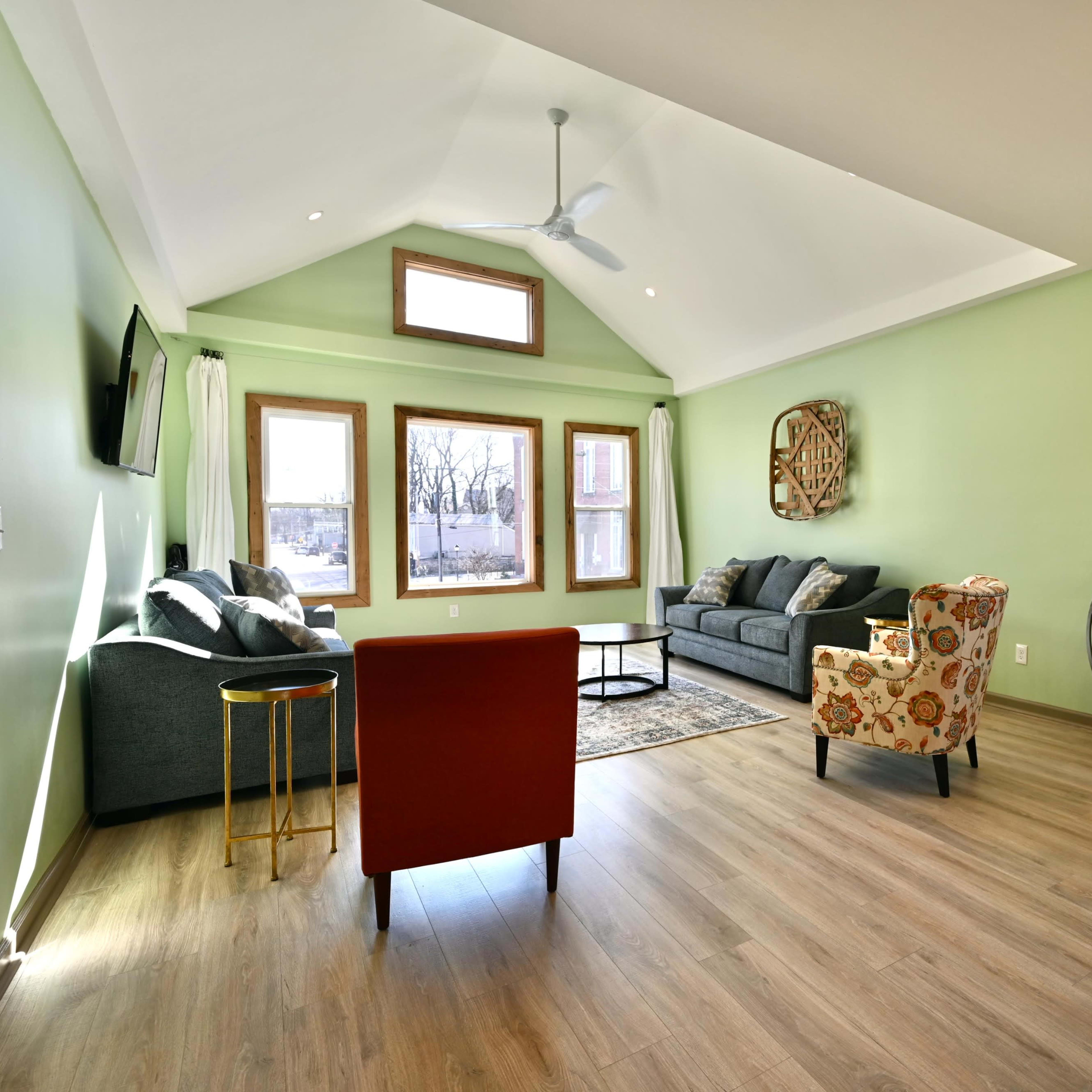 A bright living room features a green wall, modern furniture, and large windows allowing natural light to enter.