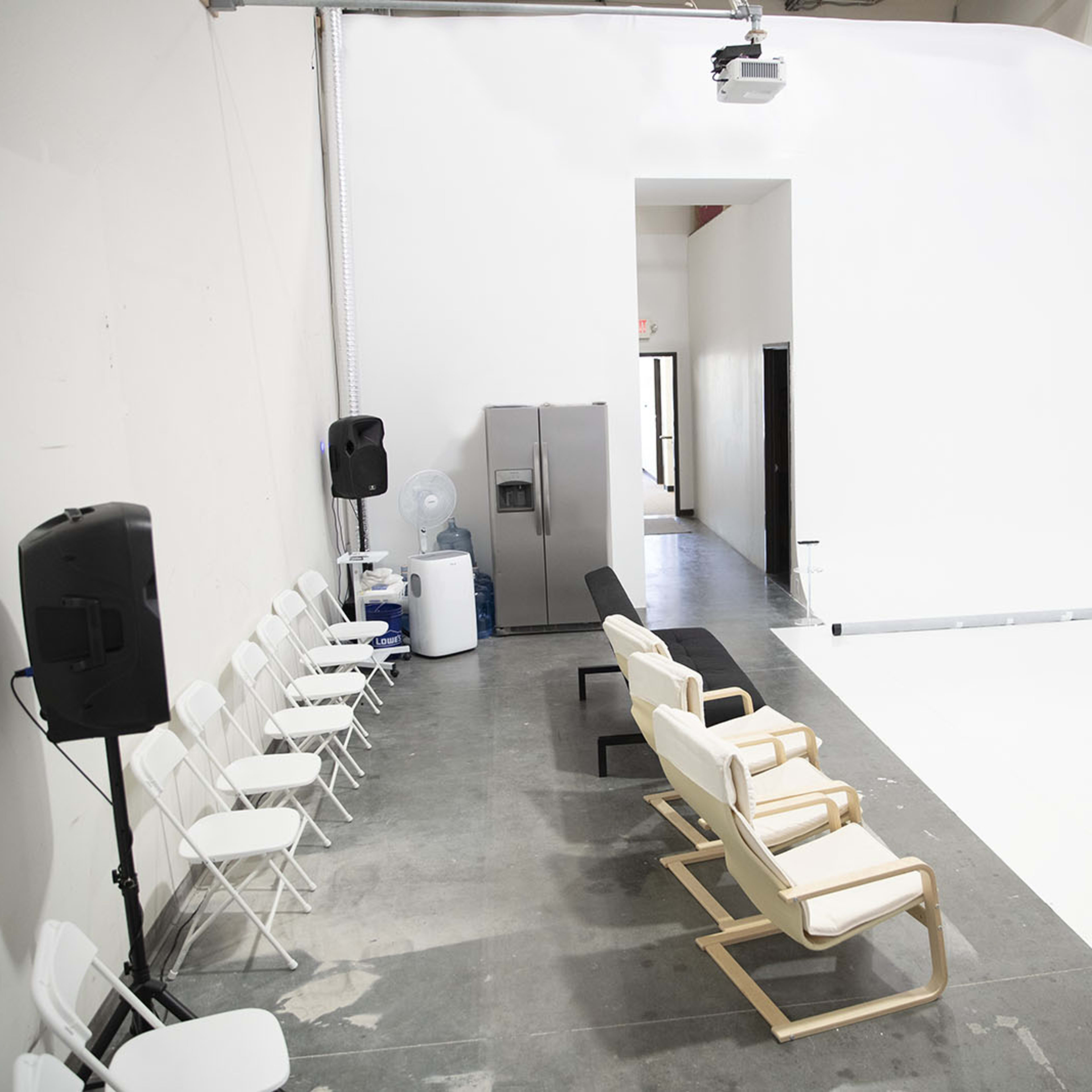 A spacious studio featuring a row of white chairs, a black bench, and a projection of a cityscape on a white wall.