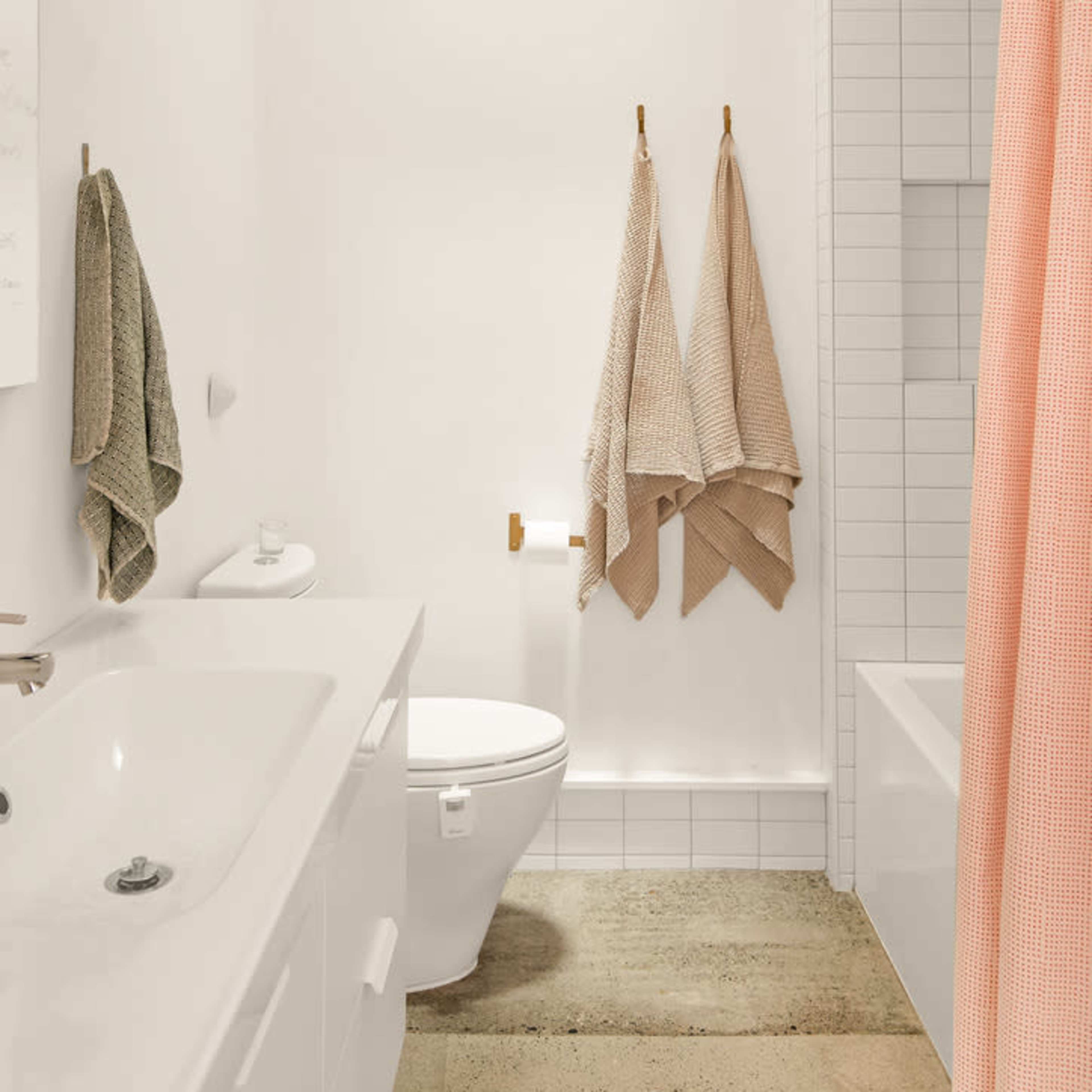 A modern bathroom with a bathtub, a toilet, a sink, and two towels hanging on a wall, illuminated by natural light from a skylight.