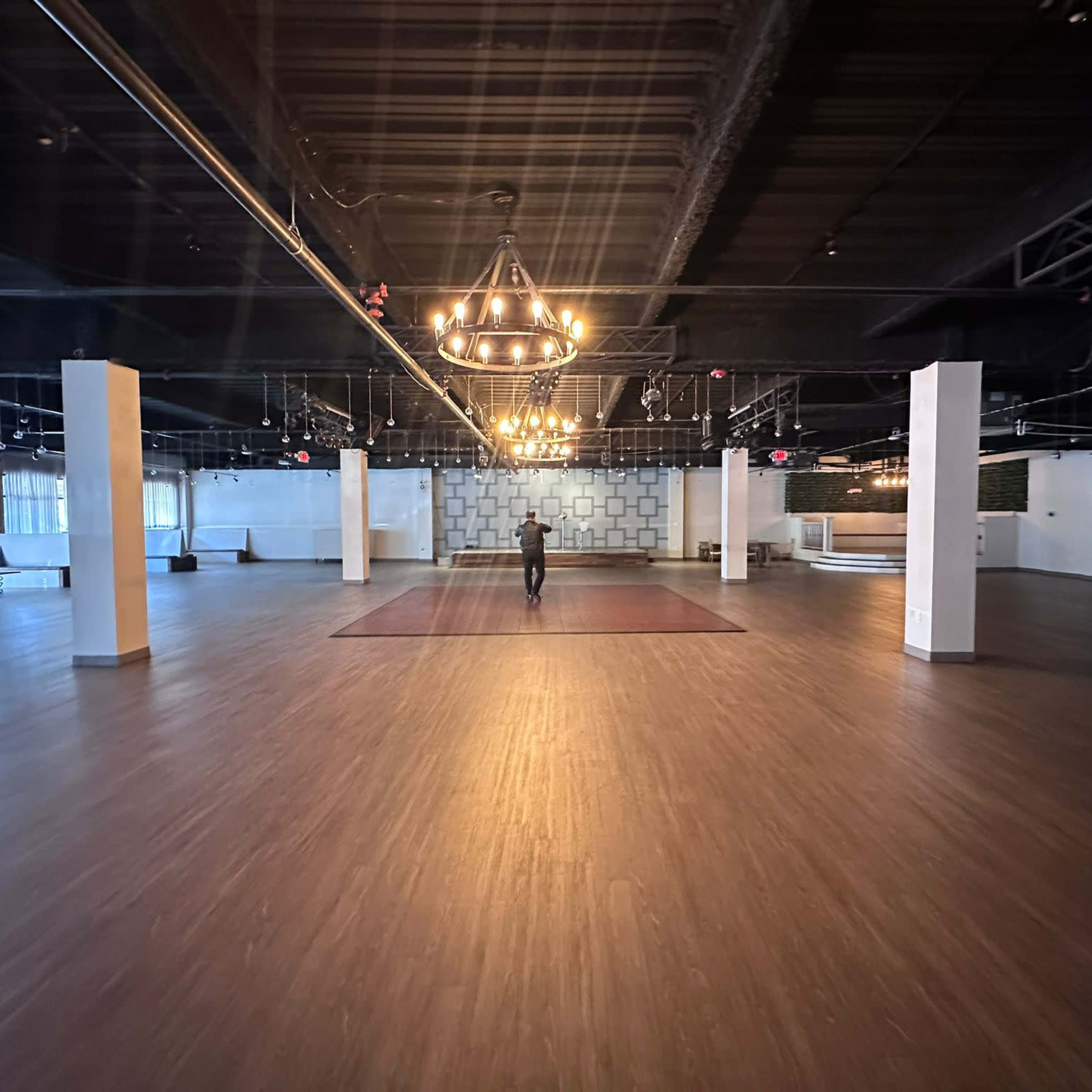 A person walks across a spacious, empty event hall with wooden flooring and decorative lighting.